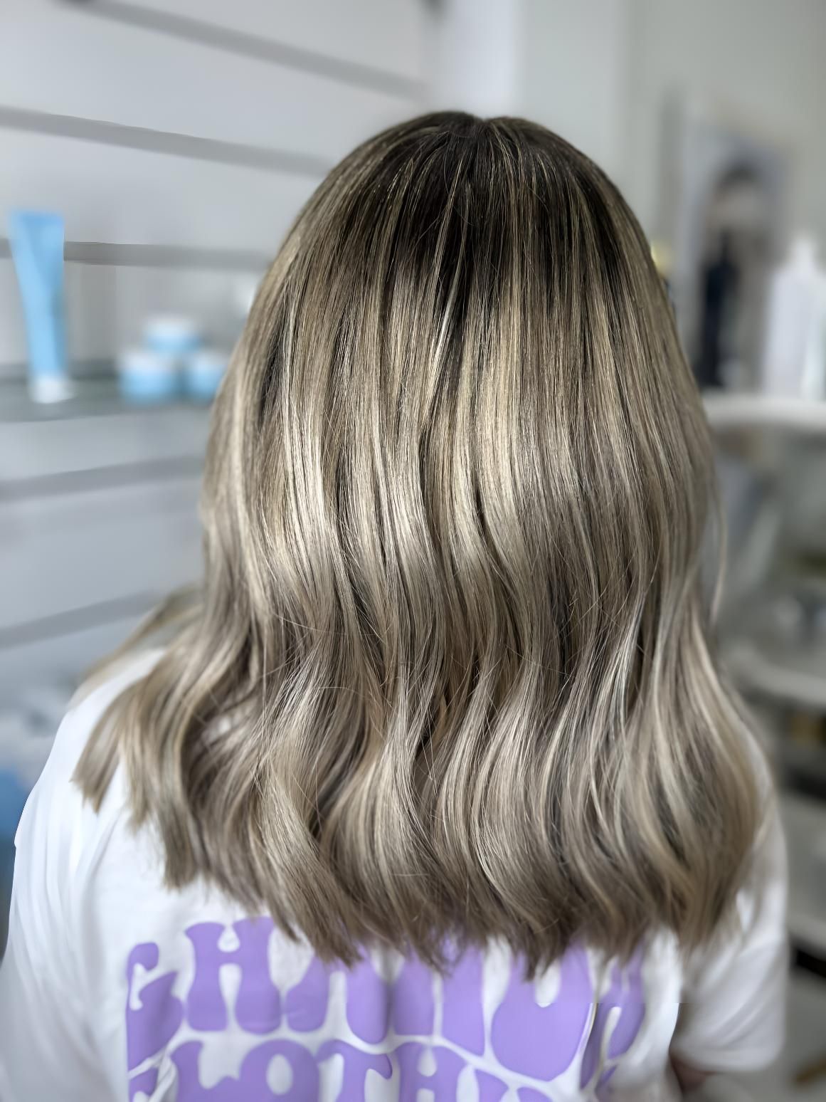 A Woman With Blonde Hair is Wearing a Purple Shirt — Strut Hair & Beauty In Maroochydore, QLD
