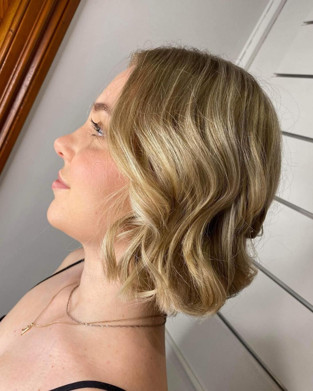 A Woman With Blonde Hair is Wearing a Black Top and a Necklace — Strut Hair & Beauty In Maroochydore, QLD