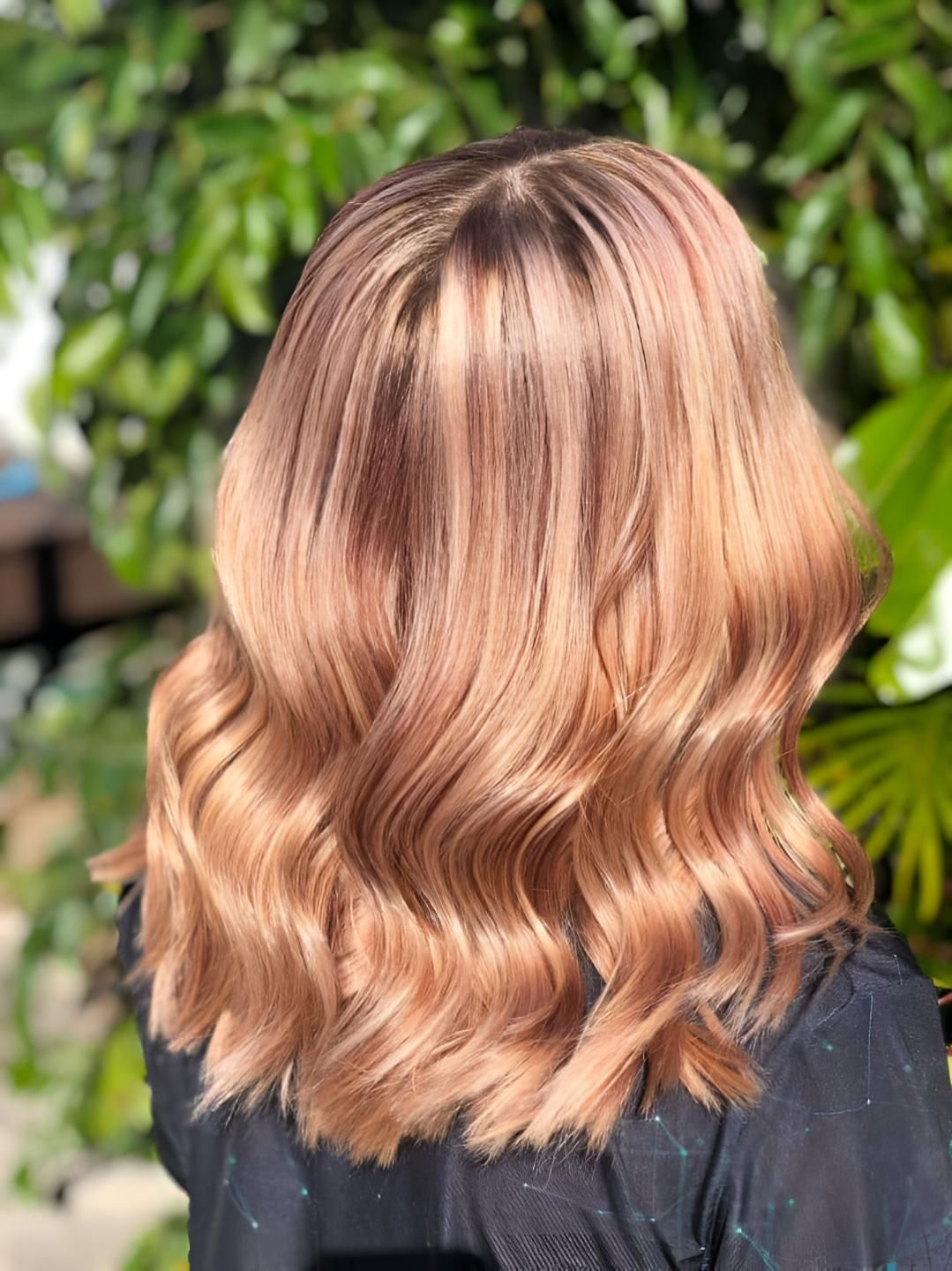 A Woman With Long Wavy Blonde Hair is Standing in Front of a Tree — Strut Hair & Beauty In Maroochydore, QLD
