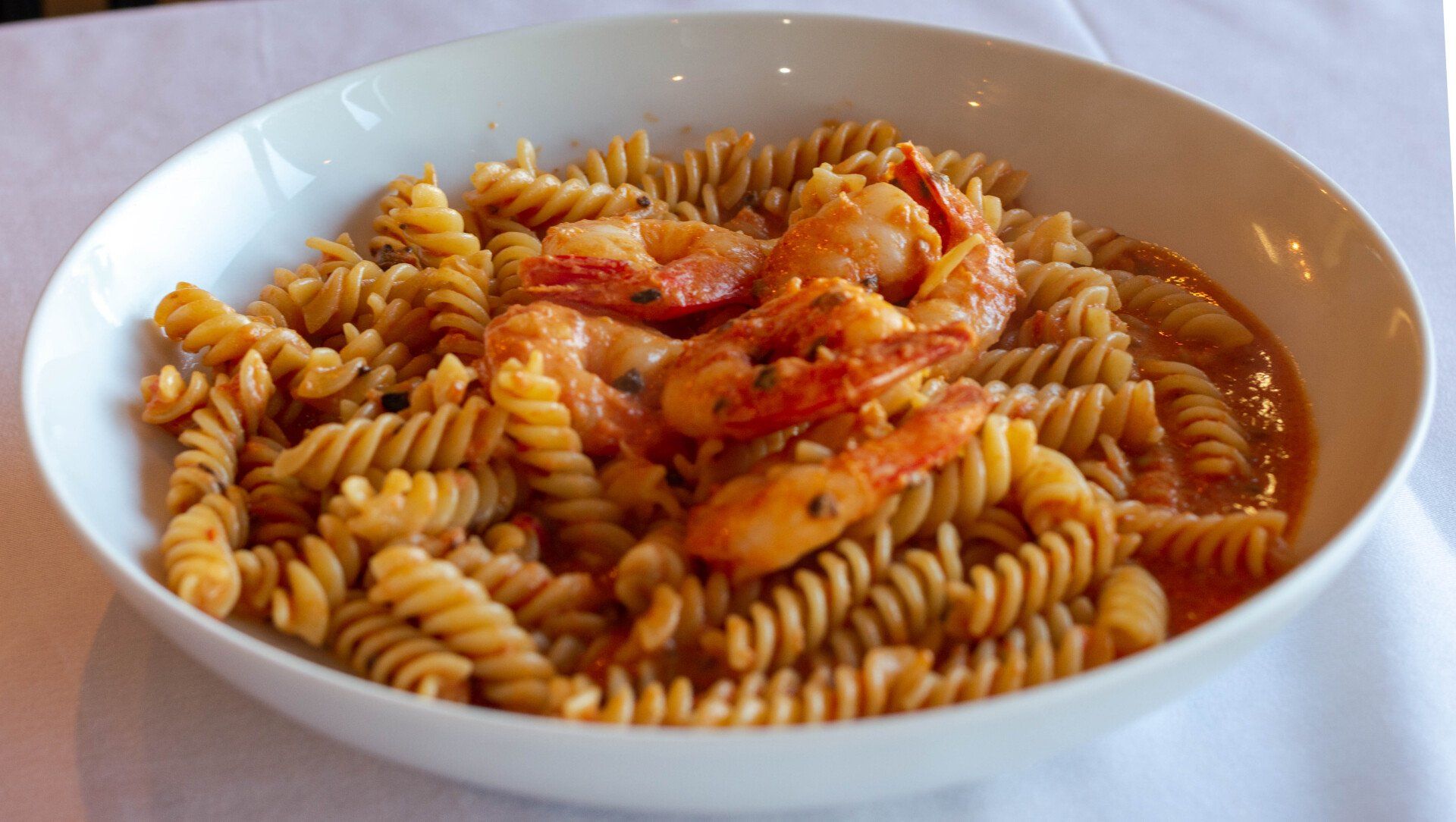 a white bowl filled with pasta and shrimp on a table