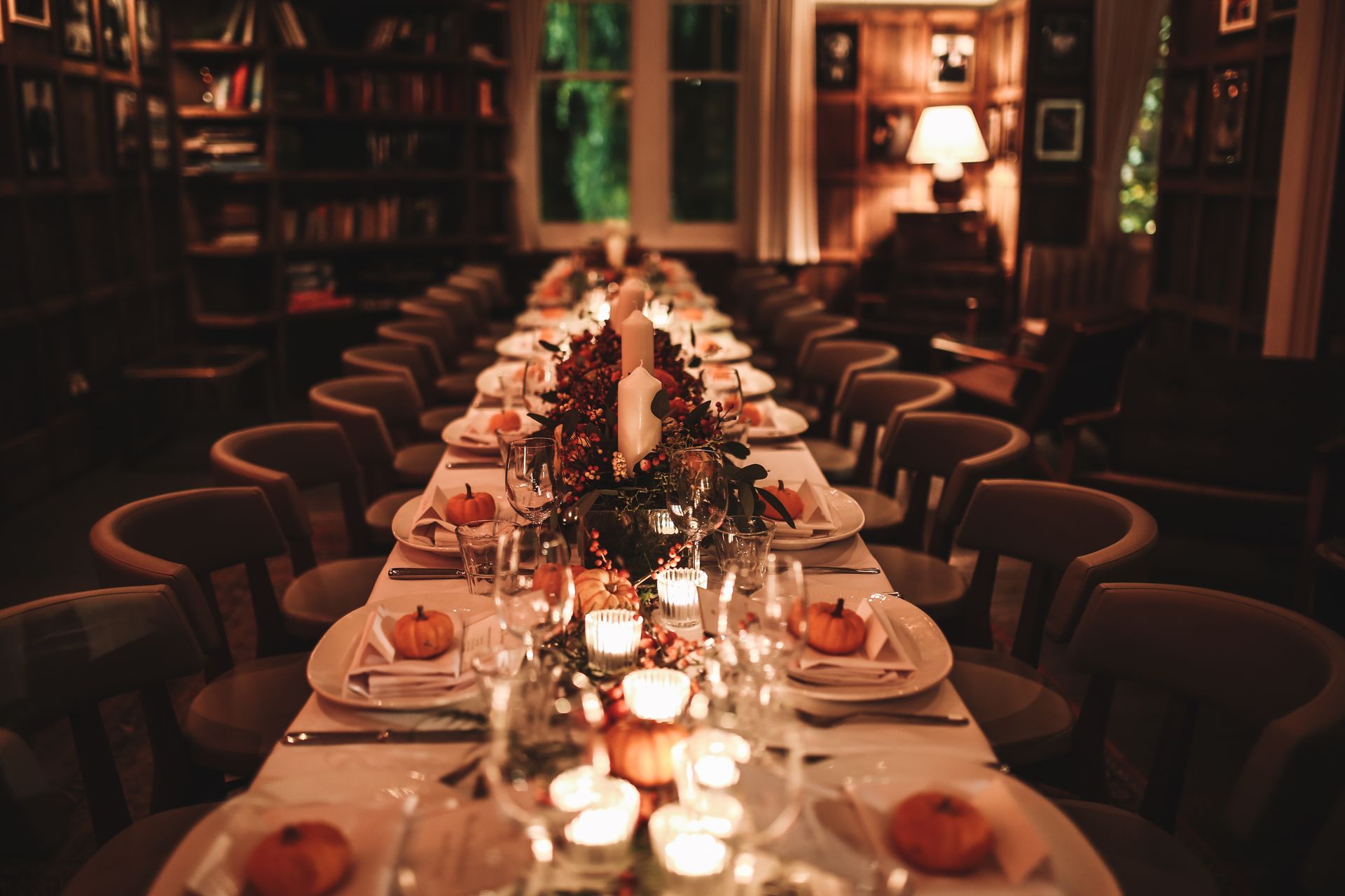 a long table with plates, glasses, candles and pumpkins on it