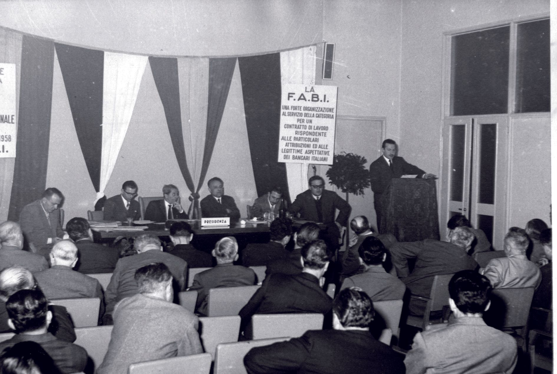 Un gruppo di persone è seduto in una stanza con un cartello che dice la pabl