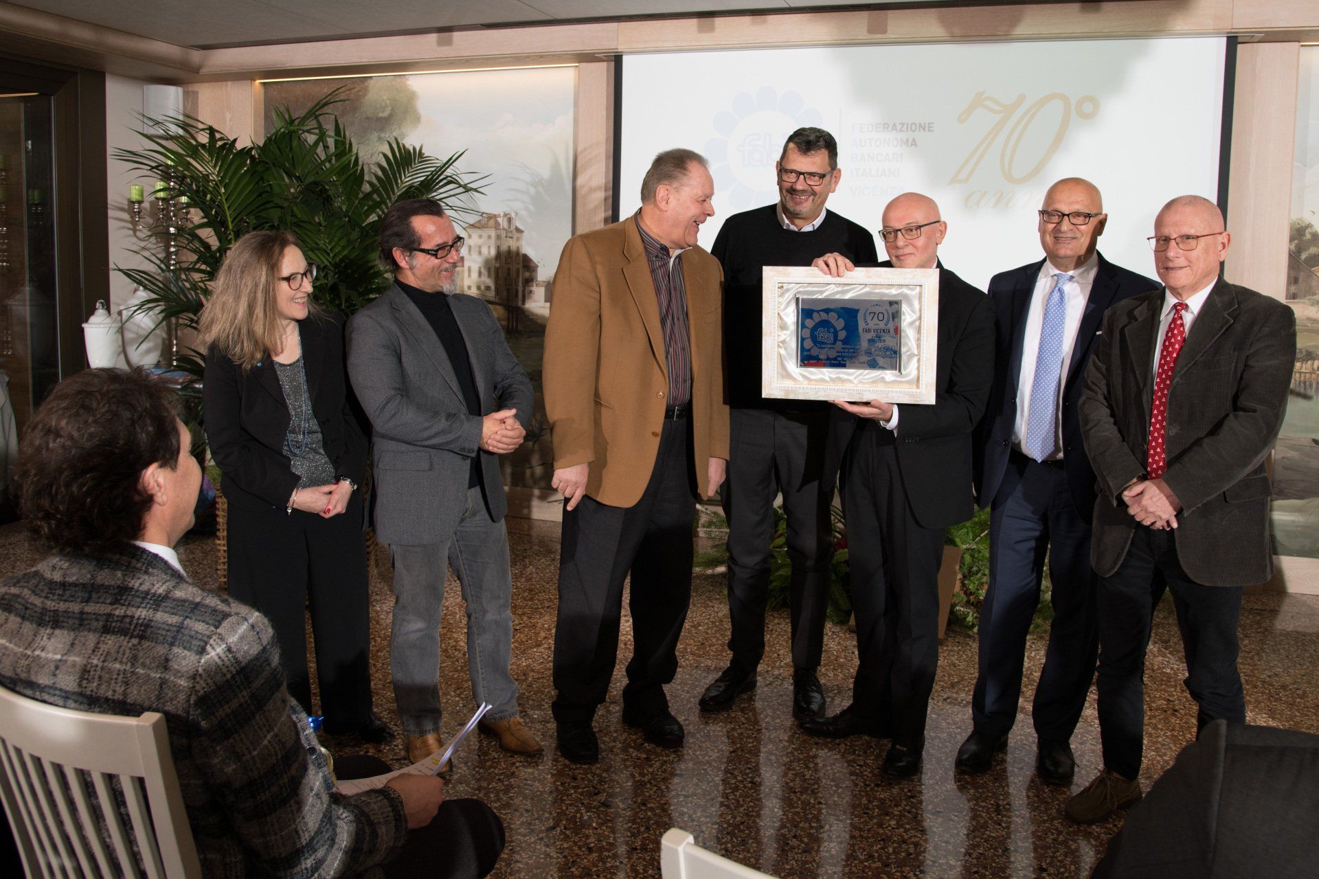 Un gruppo di uomini sta in piedi attorno a un uomo che tiene in mano una foto incorniciata.
