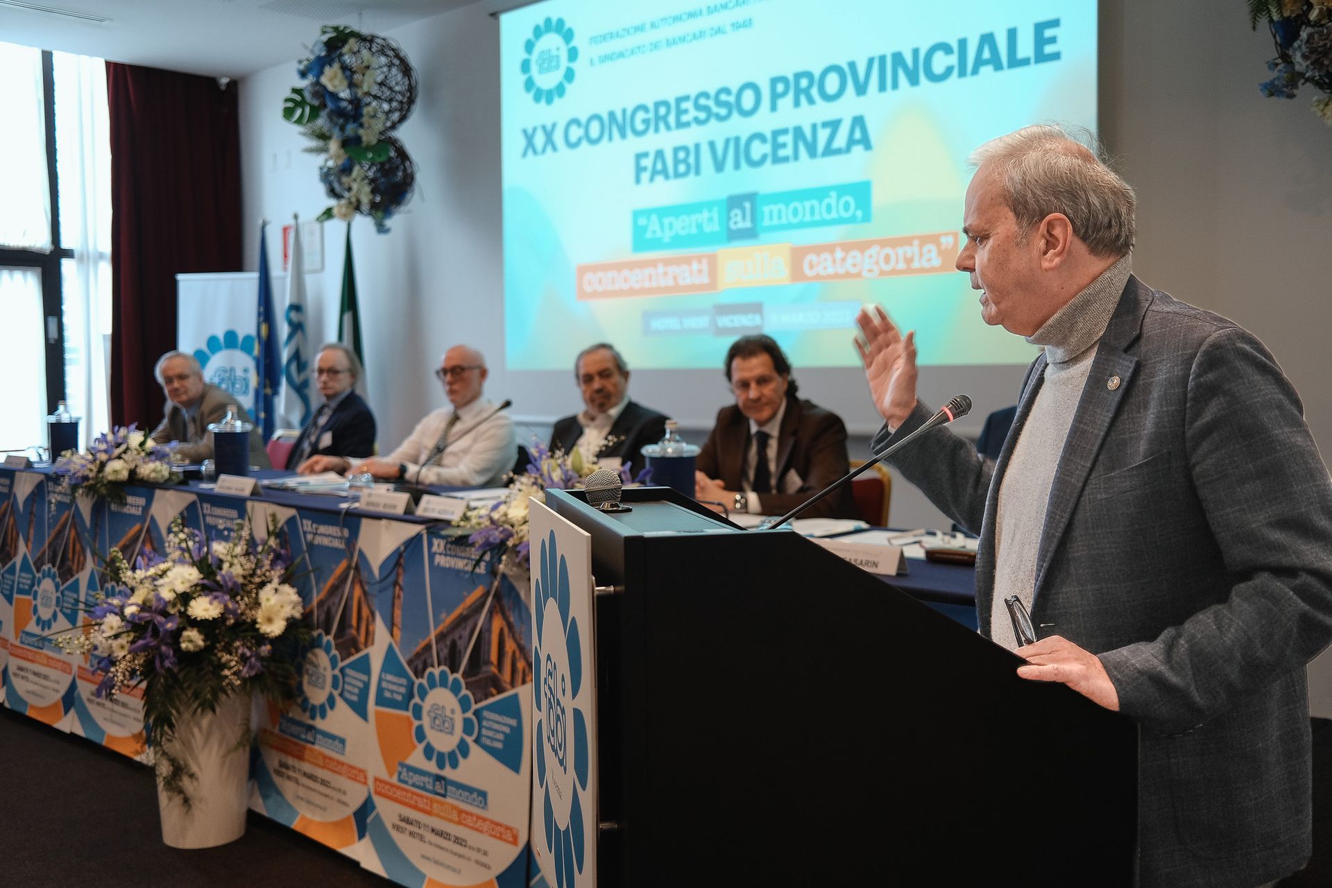 Un uomo è in piedi su un podio e tiene un discorso davanti a un gruppo di persone.