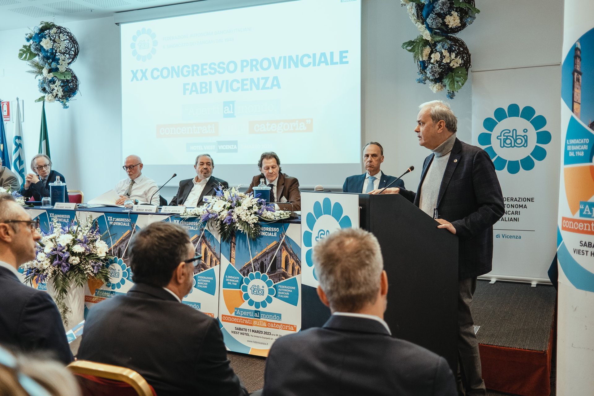 Un uomo è in piedi su un podio e tiene un discorso davanti a un gruppo di persone.