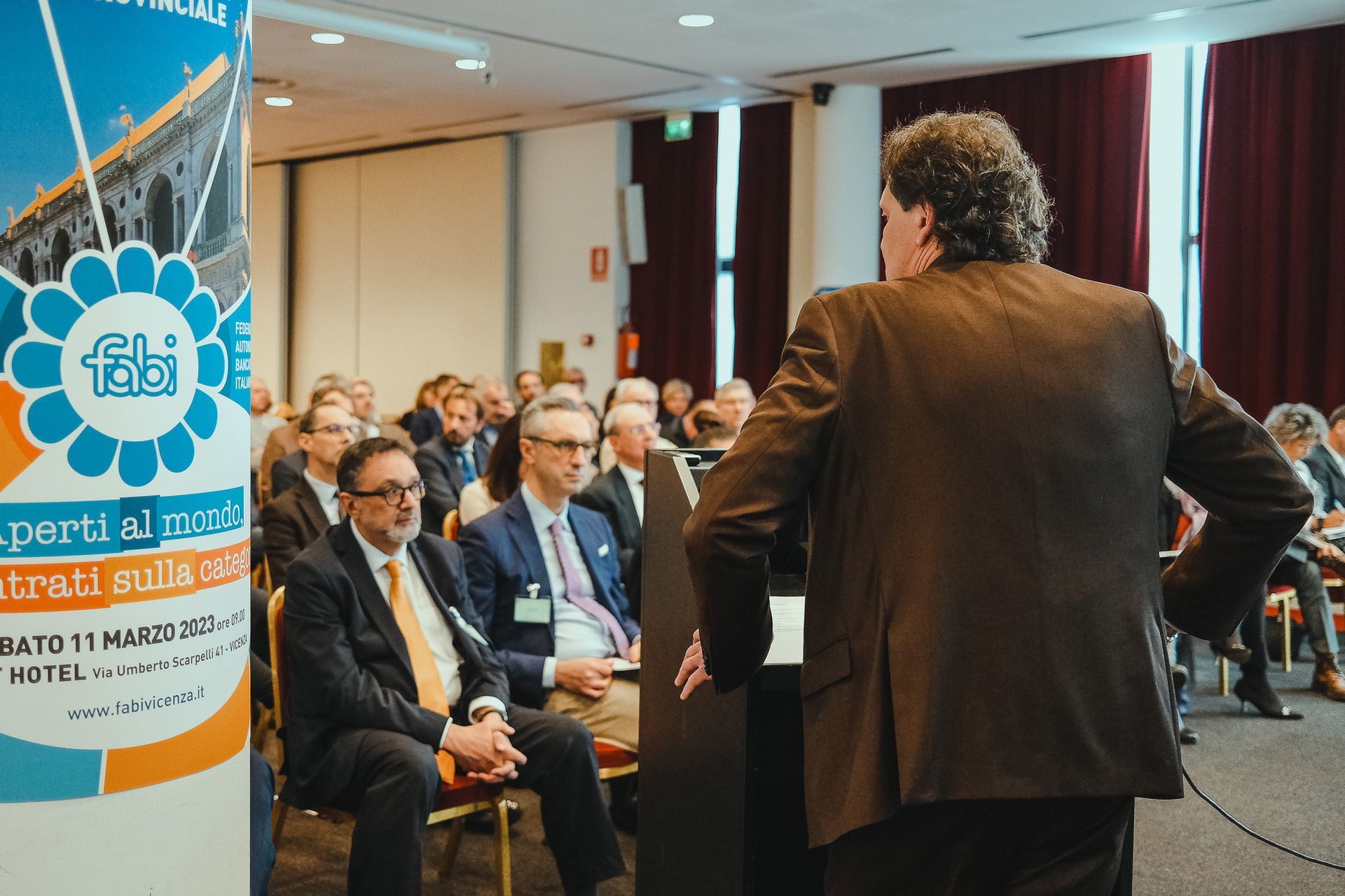 Un uomo in giacca e cravatta è in piedi di fronte a un gruppo di persone sedute su sedie.