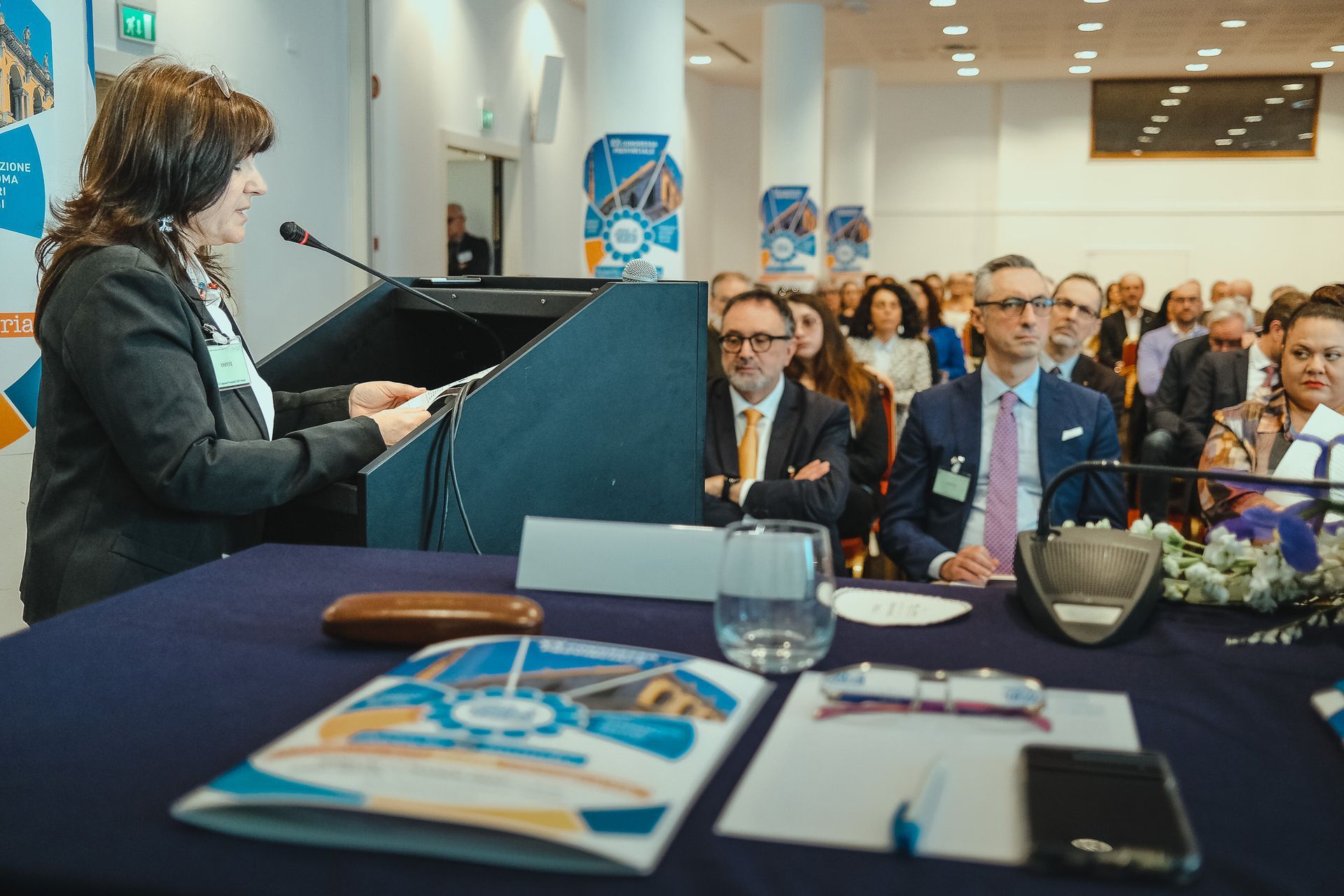 Una donna è in piedi su un podio e fa una presentazione a un gruppo di persone.