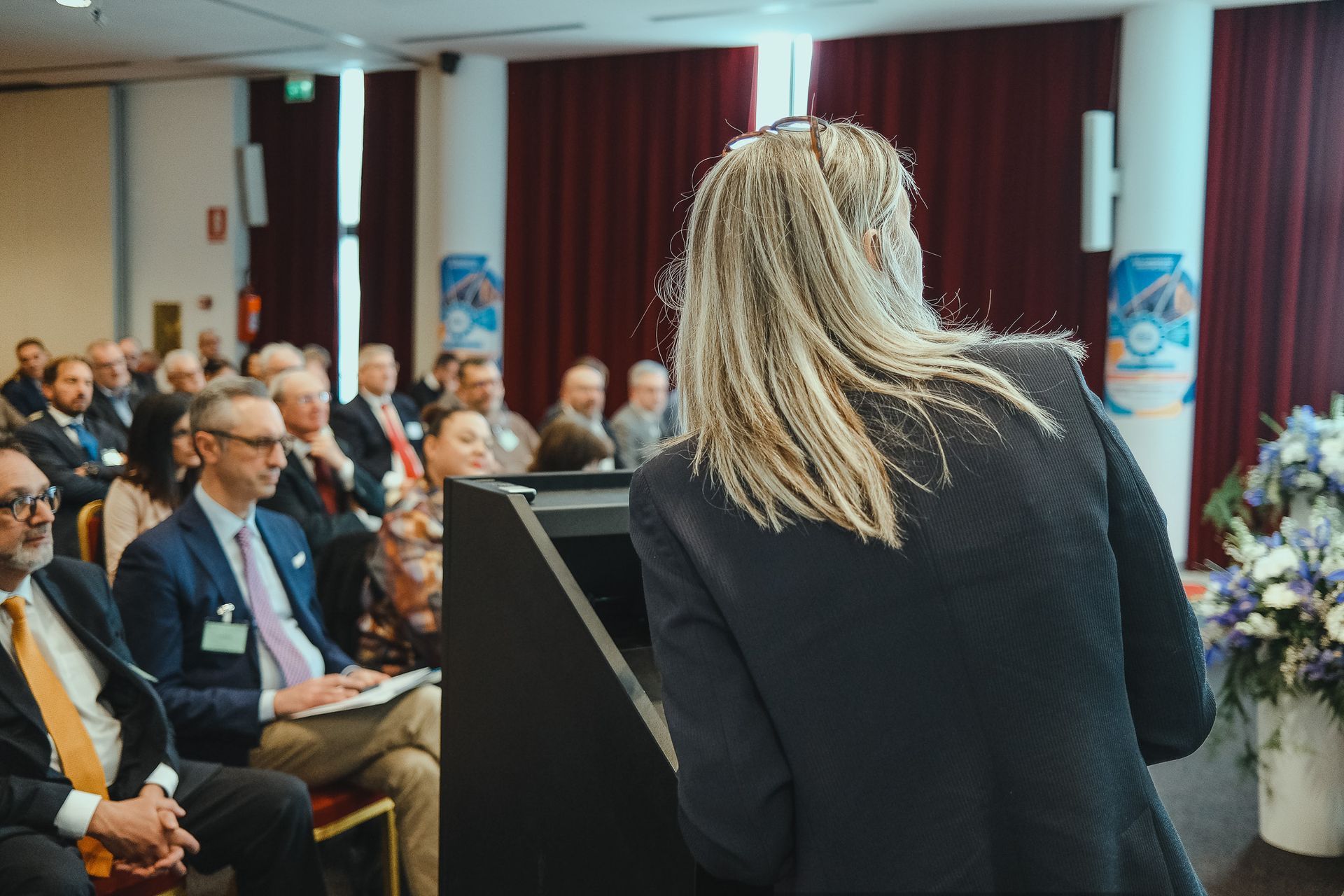 Una donna è in piedi su un podio e fa una presentazione a un gruppo di persone.