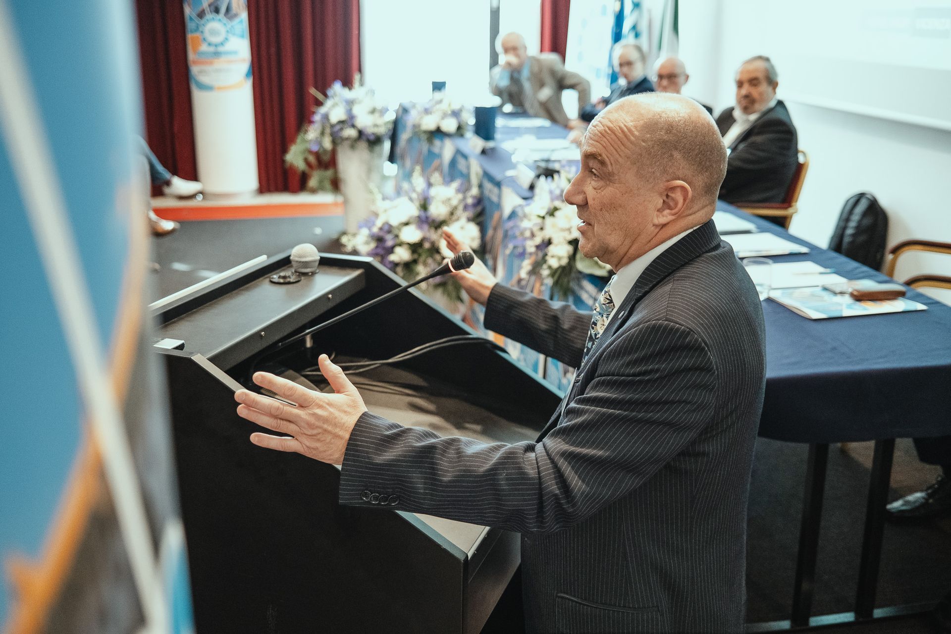 Un uomo in giacca e cravatta tiene un discorso su un podio.