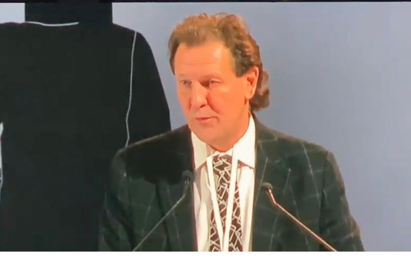 Un uomo in giacca e cravatta parla al microfono.