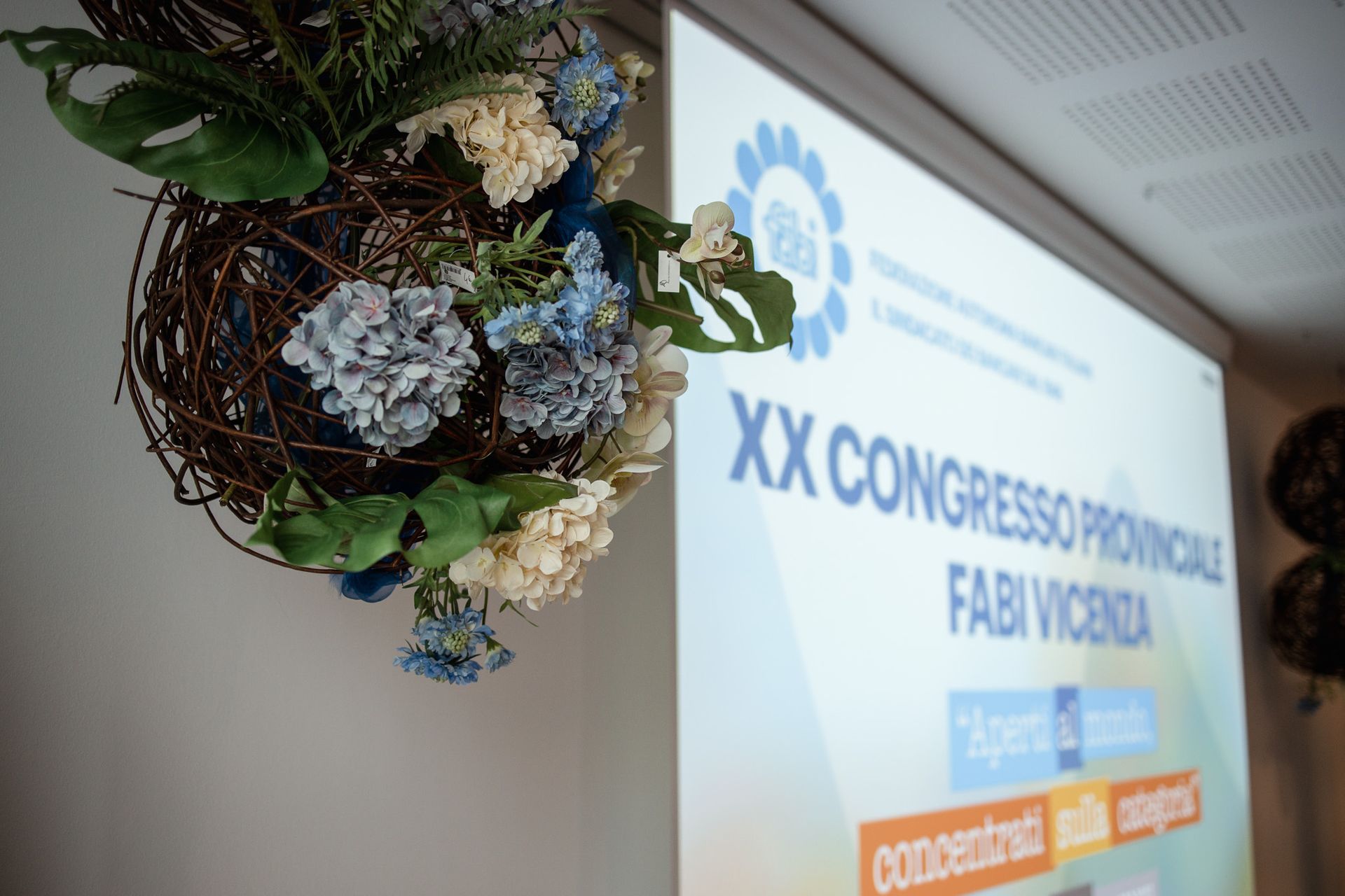 Fiori pendono dal soffitto davanti allo schermo del proiettore con la scritta xx congresso provinciale fabi vicenza