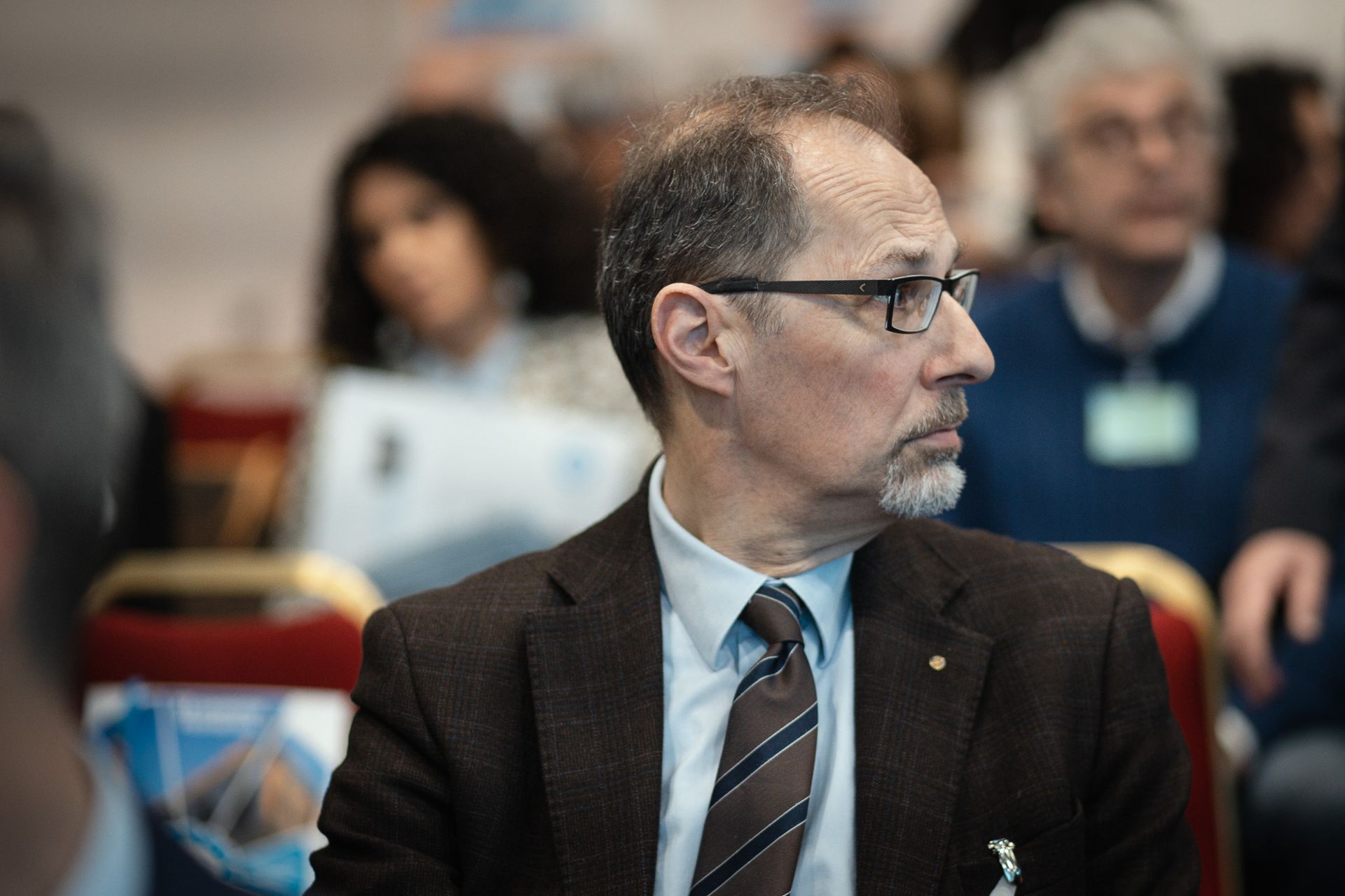 Un uomo in giacca e cravatta è seduto in una stanza con altre persone.