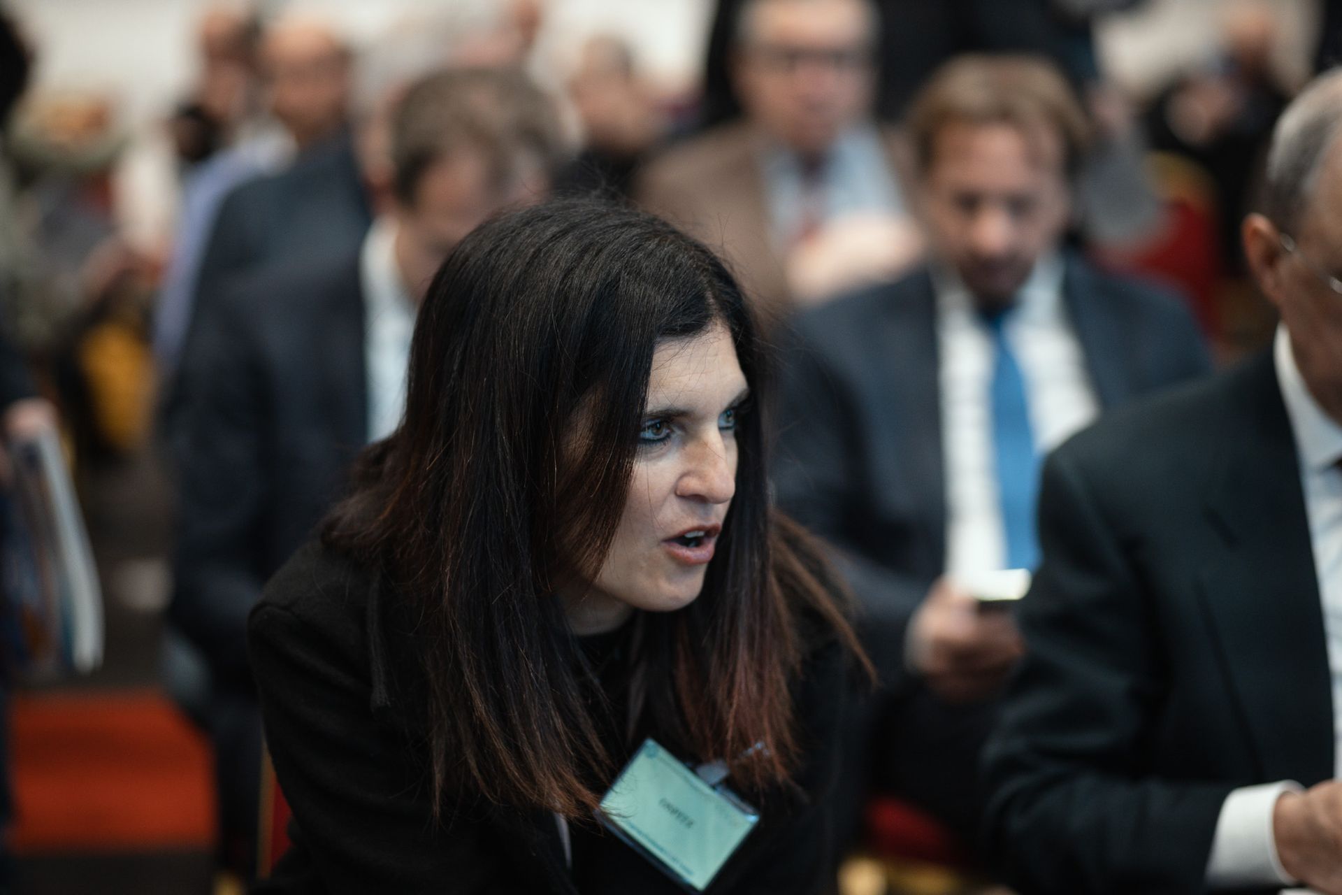 Una donna che indossa una targhetta con il nome è seduta in mezzo a una folla di persone.