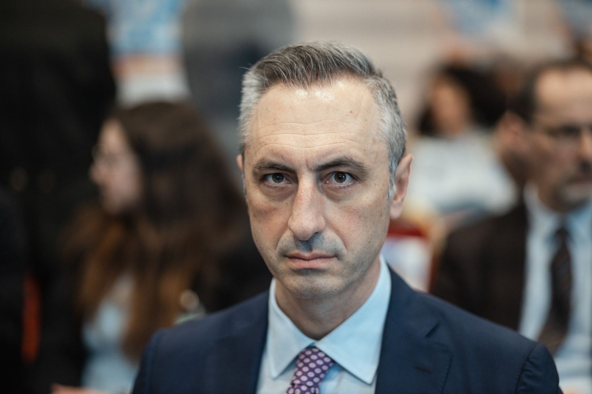 Un uomo in giacca e cravatta guarda la telecamera.