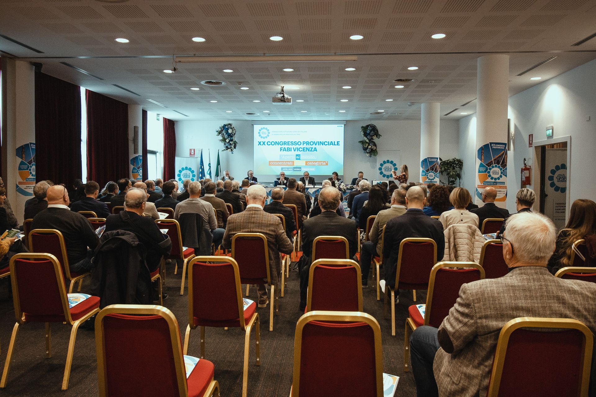 Un folto gruppo di persone è seduto in una sala conferenze e guarda una presentazione.