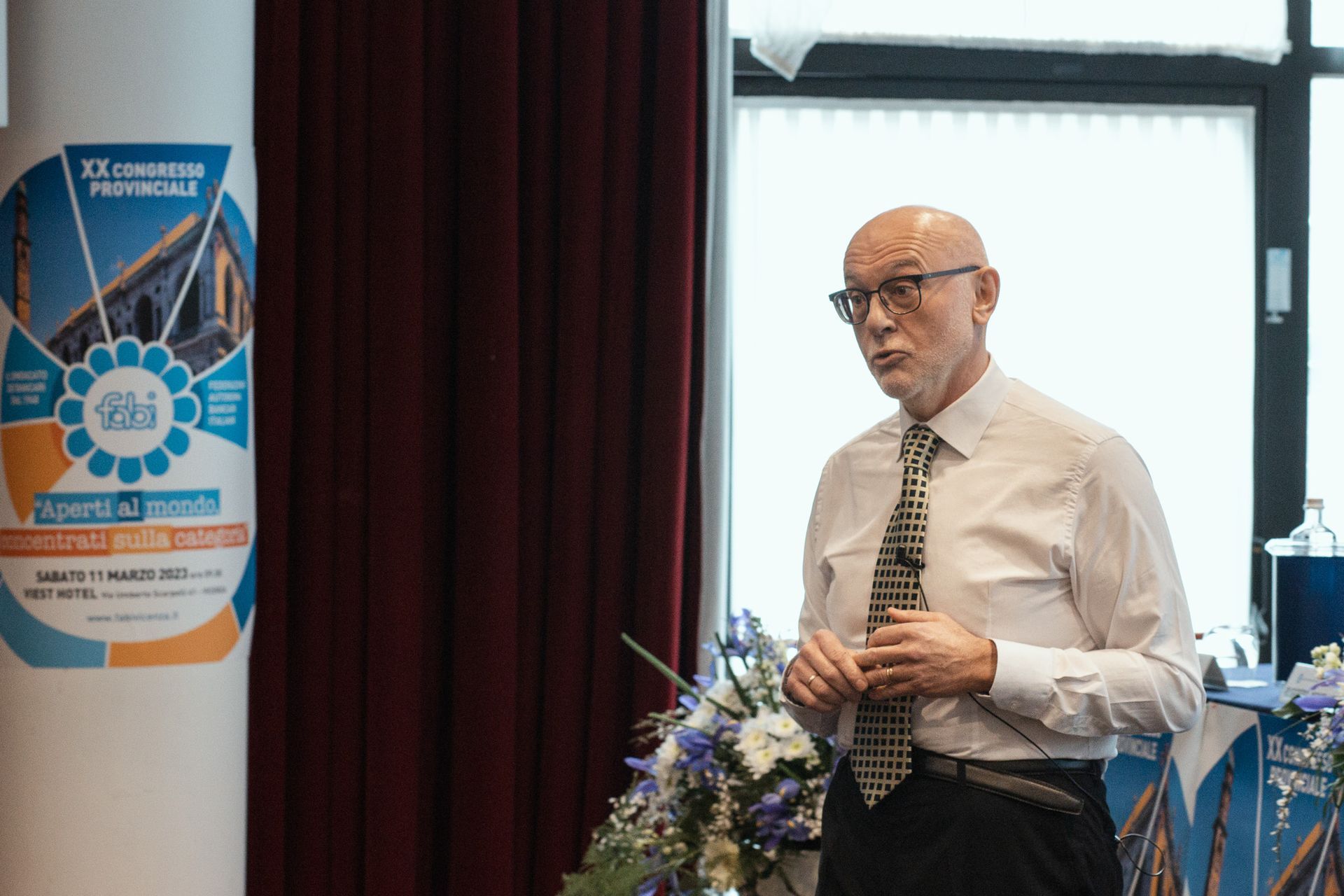 Un uomo in camicia bianca e cravatta è in piedi davanti a una finestra.