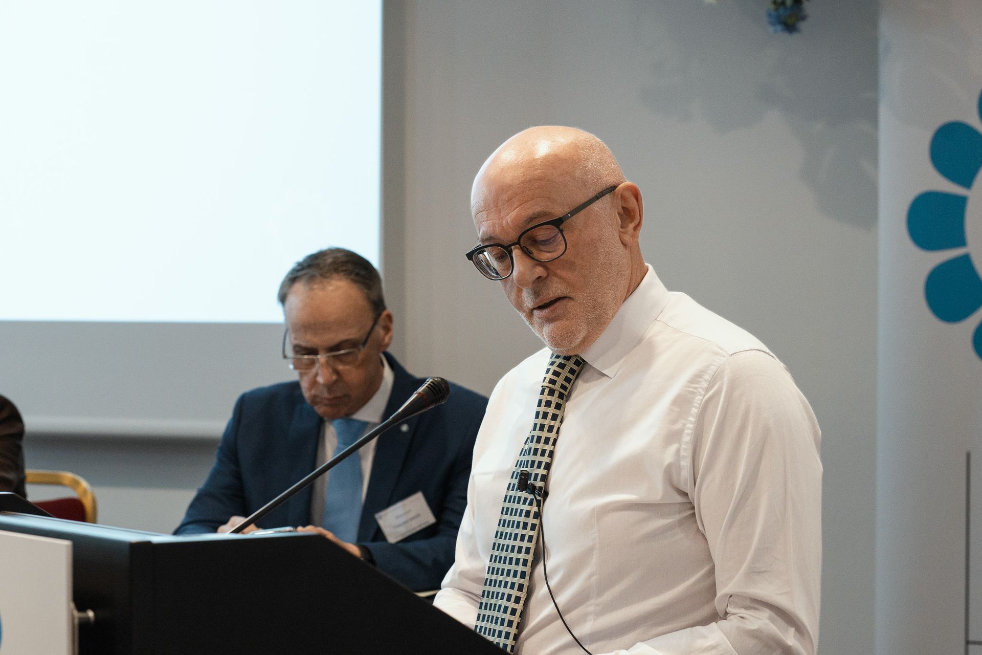 Un uomo in camicia bianca e cravatta tiene un discorso su un podio.