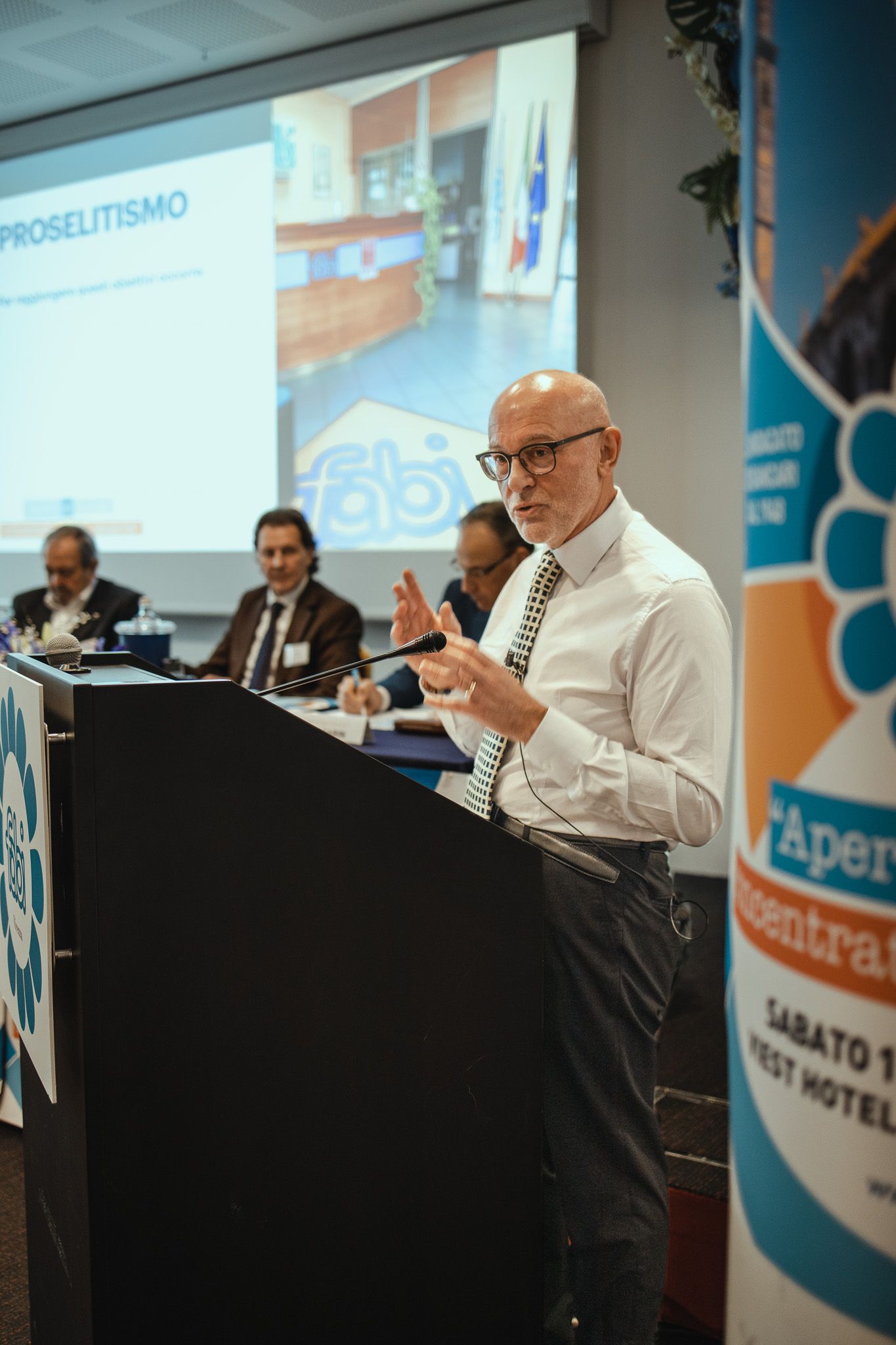 Un uomo è in piedi su un podio e fa una presentazione a un gruppo di persone.