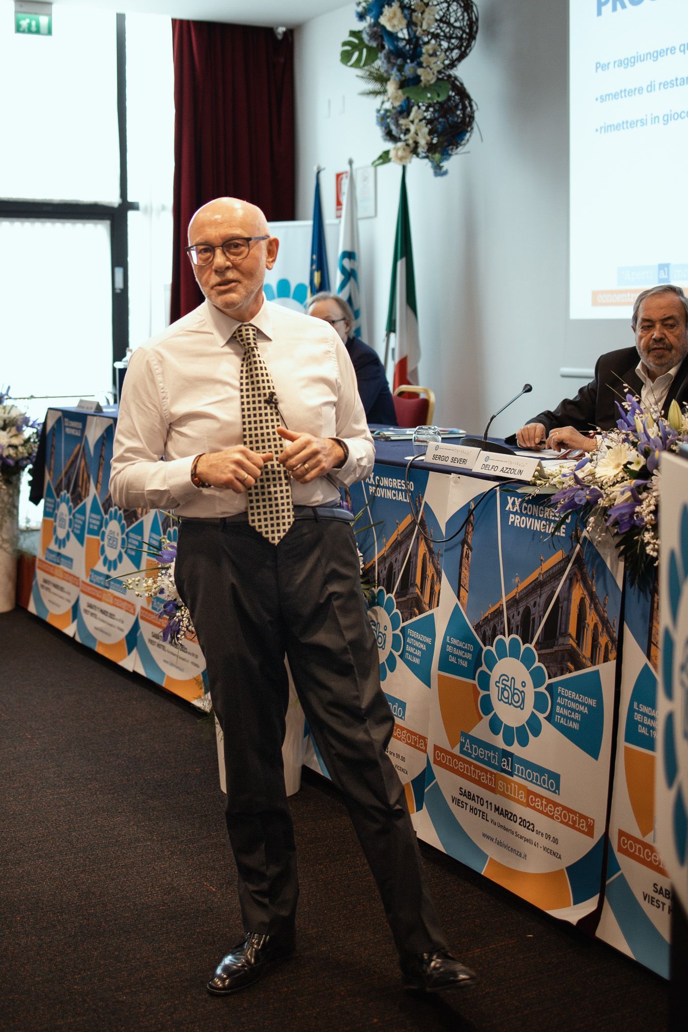 Un uomo in camicia bianca e cravatta è in piedi davanti a un tavolo con dei fiori sopra.