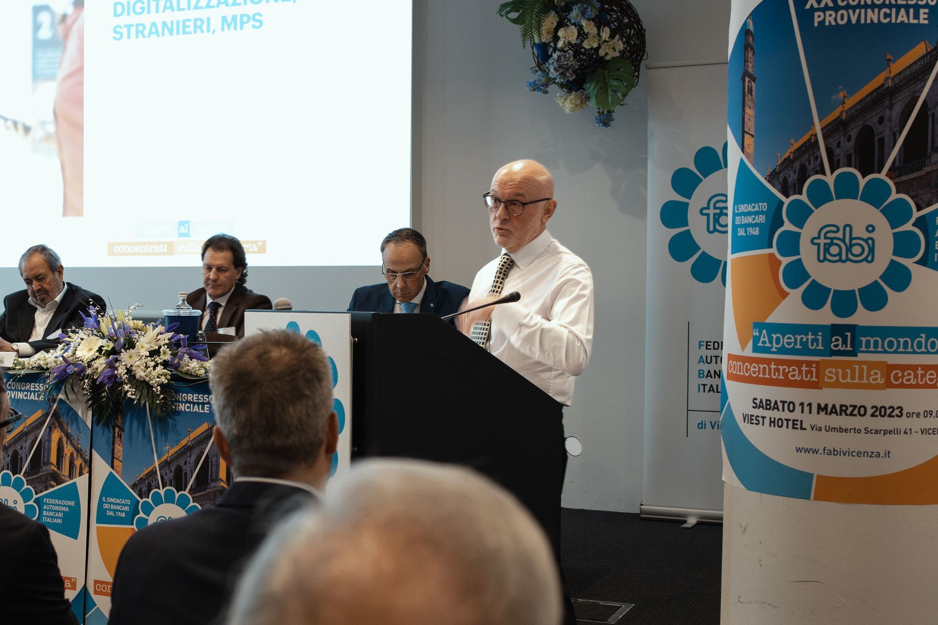 Un uomo è in piedi su un podio e tiene un discorso davanti a un gruppo di persone.