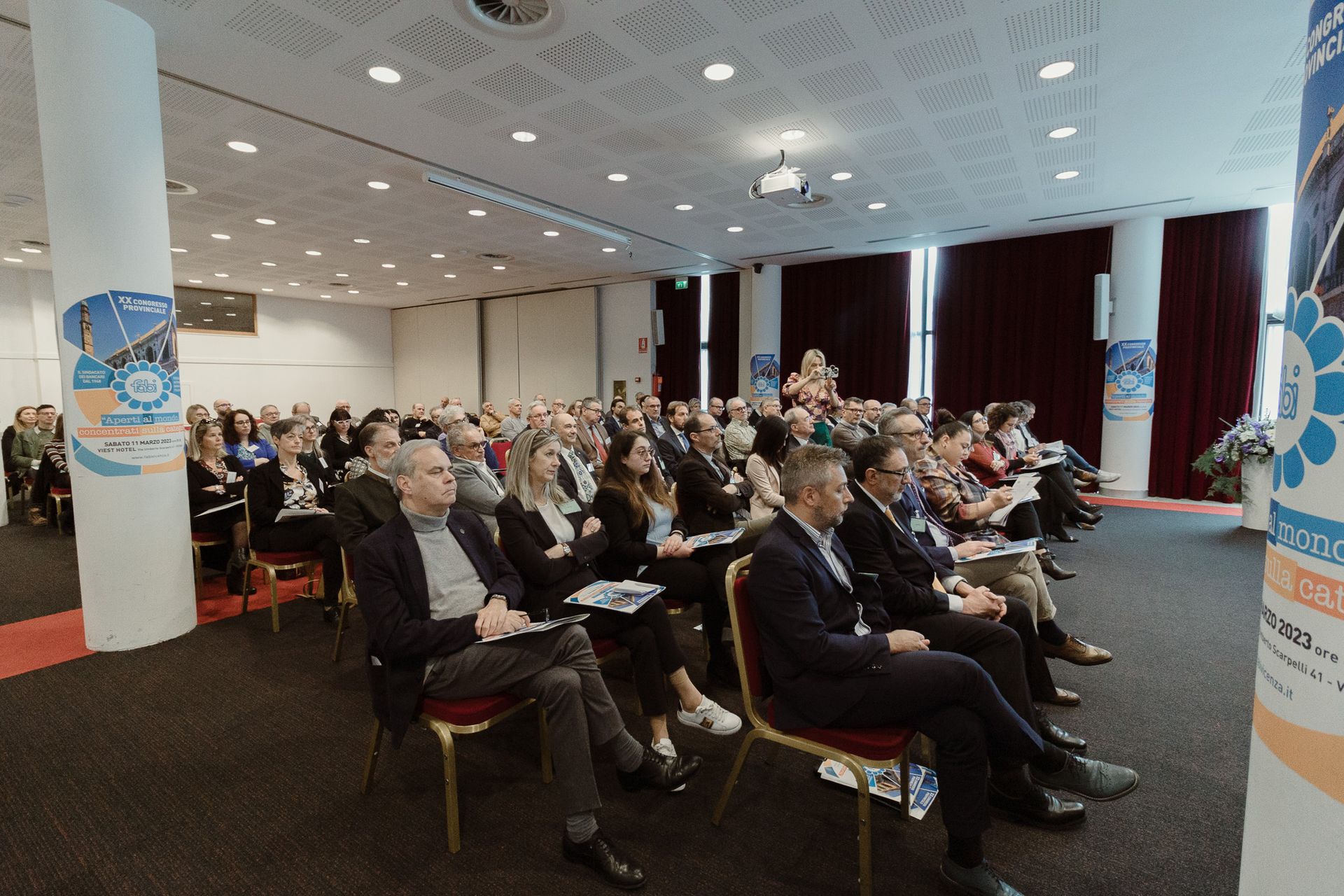 Un folto gruppo di persone è seduto in una sala conferenze.
