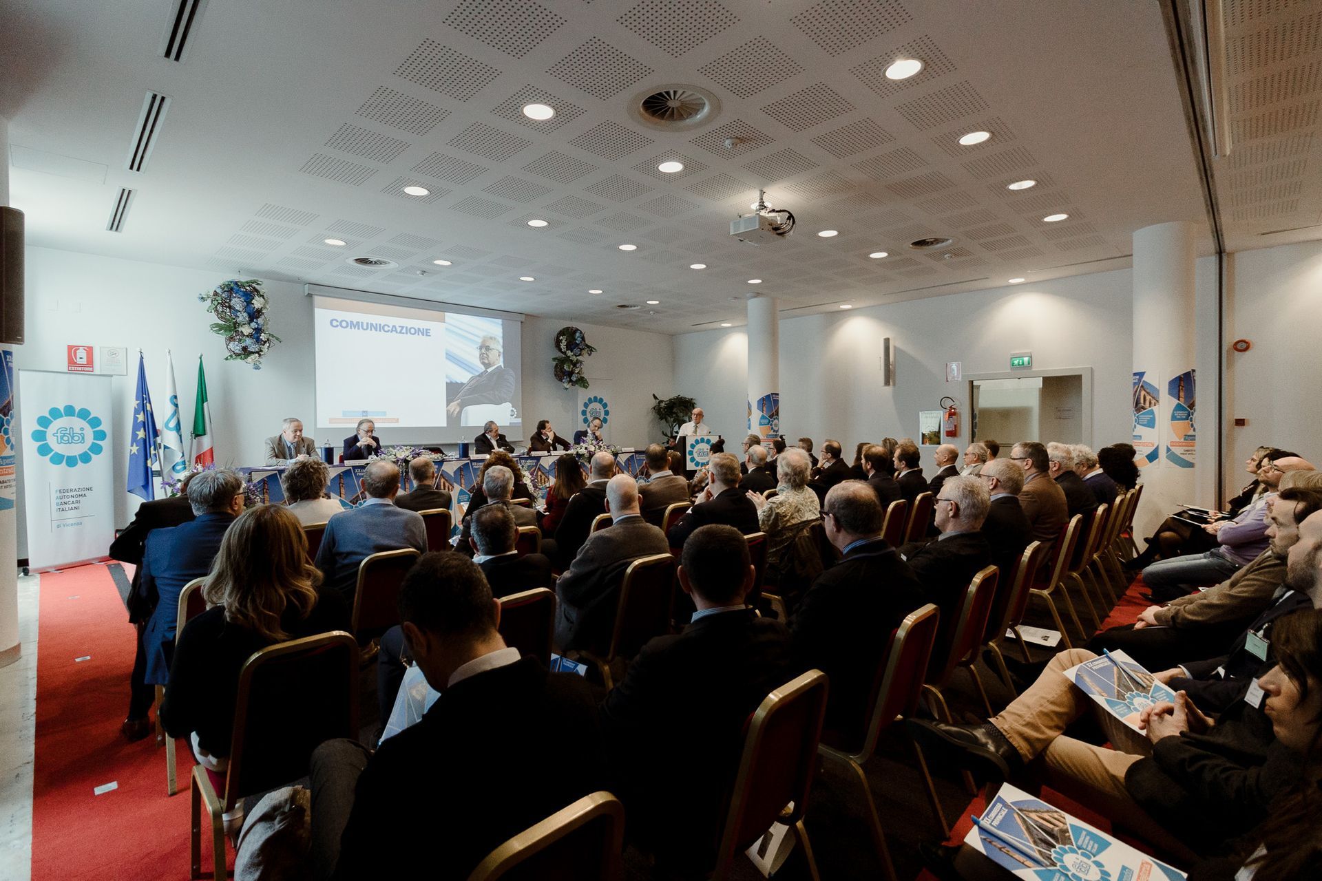 Un folto gruppo di persone è seduto in una sala conferenze e guarda una presentazione.