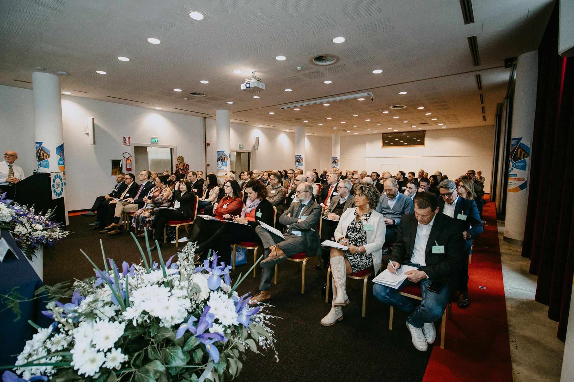 Un folto gruppo di persone è seduto sulle sedie in una sala conferenze.