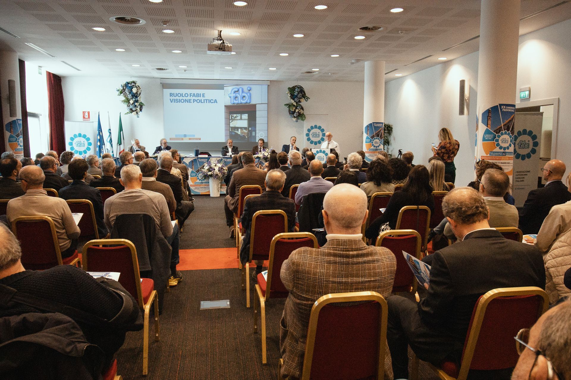 Un folto gruppo di persone è seduto in una sala conferenze e guarda una presentazione.