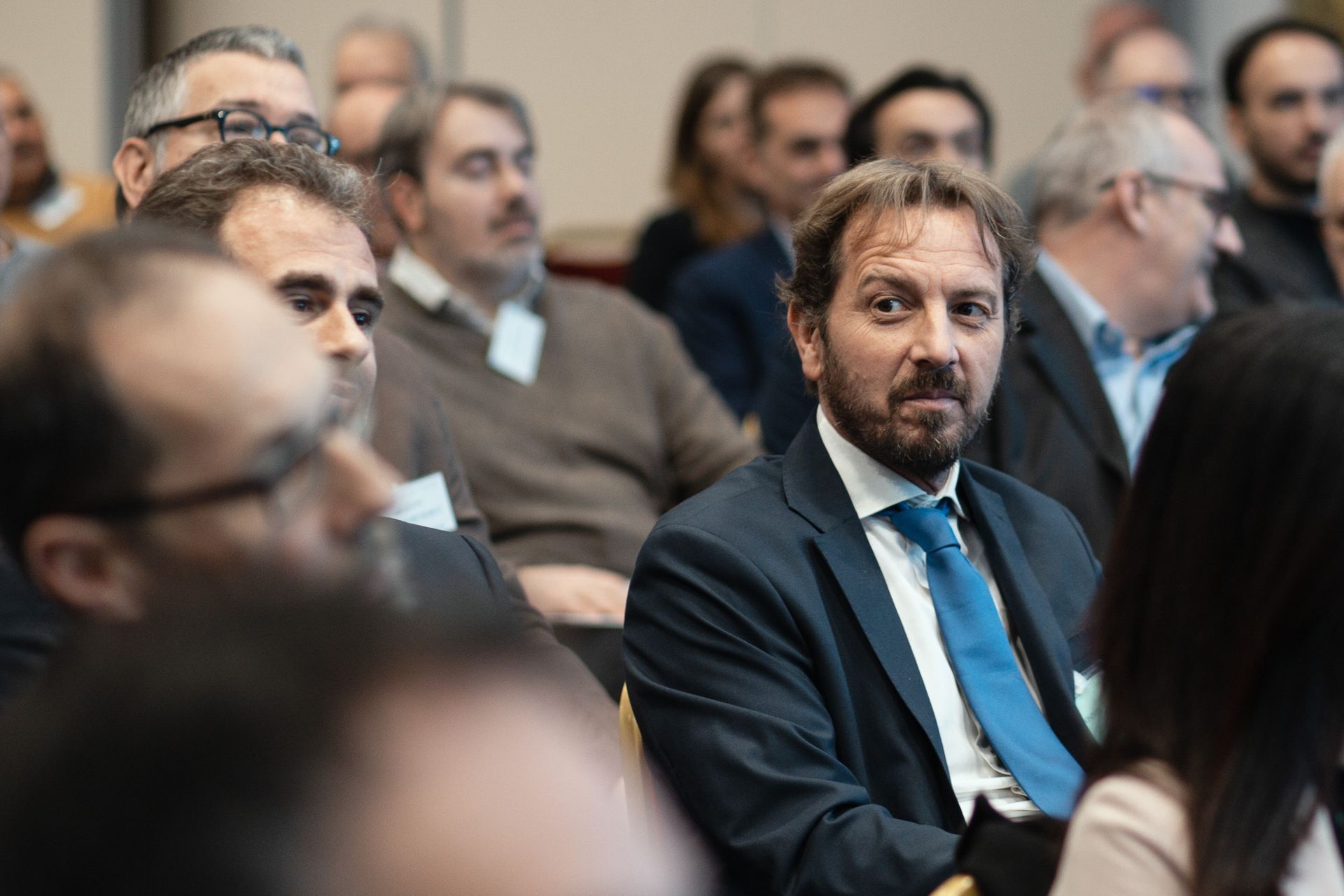 Un uomo in giacca e cravatta è seduto in mezzo a una folla di persone.