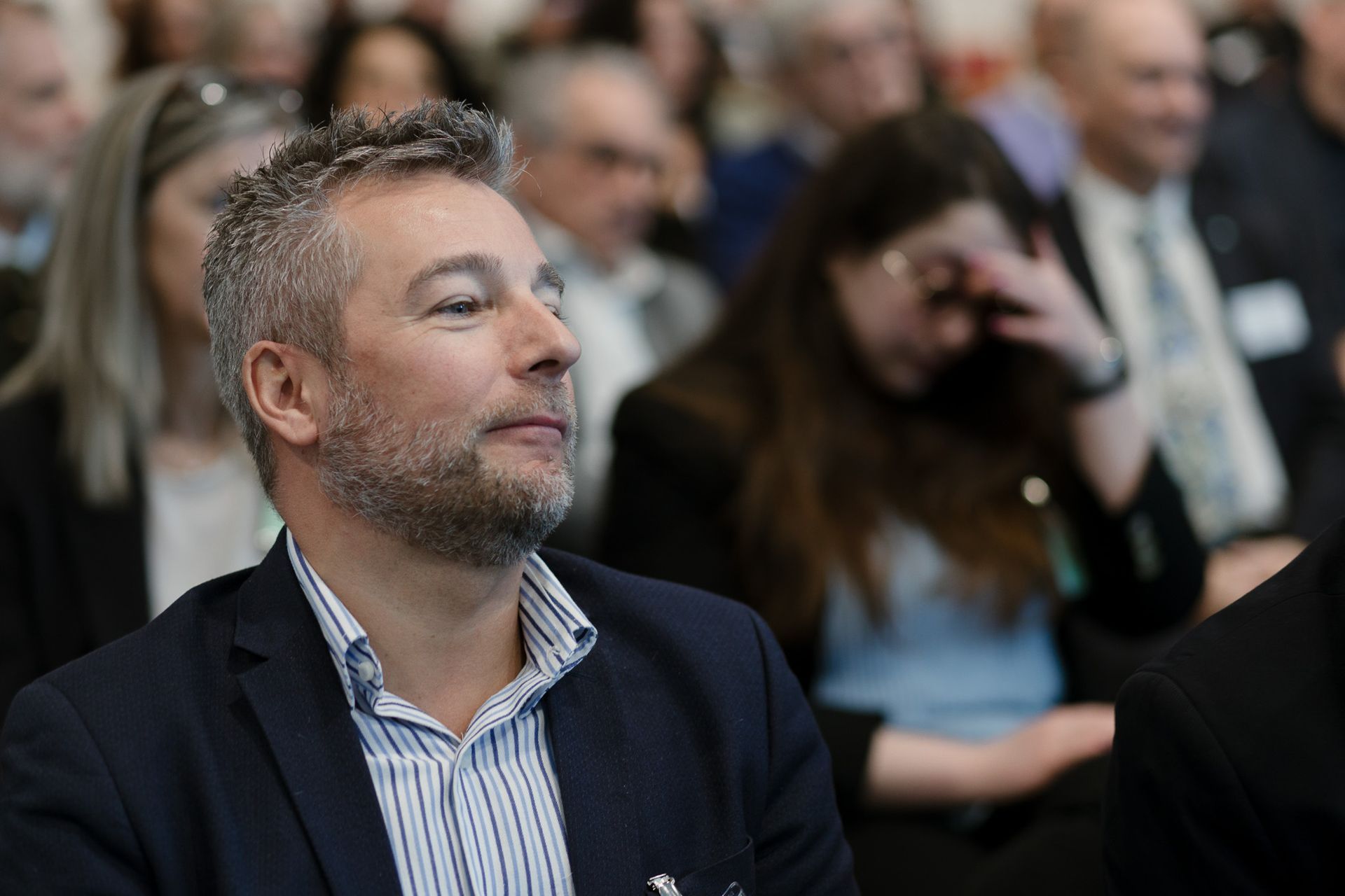 Un uomo con la barba è seduto in mezzo a una folla di persone.