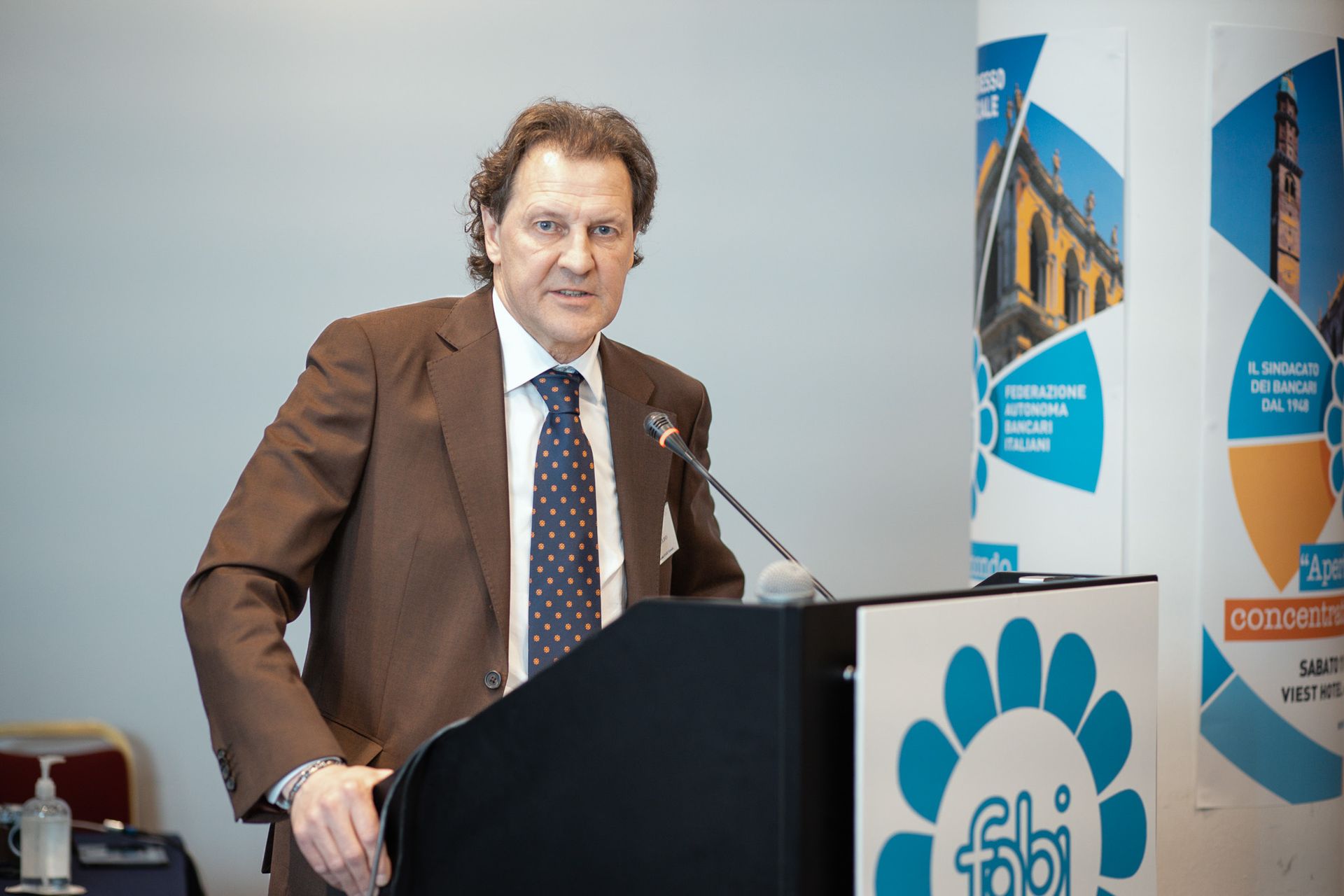 Un uomo in giacca e cravatta è in piedi su un podio con un microfono.