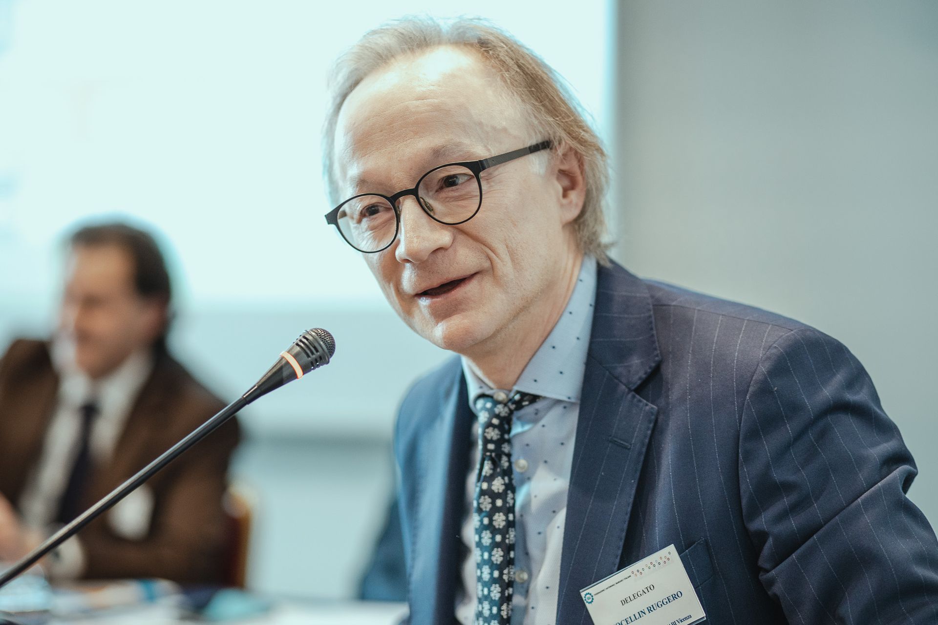 Un uomo in giacca e cravatta parla al microfono.