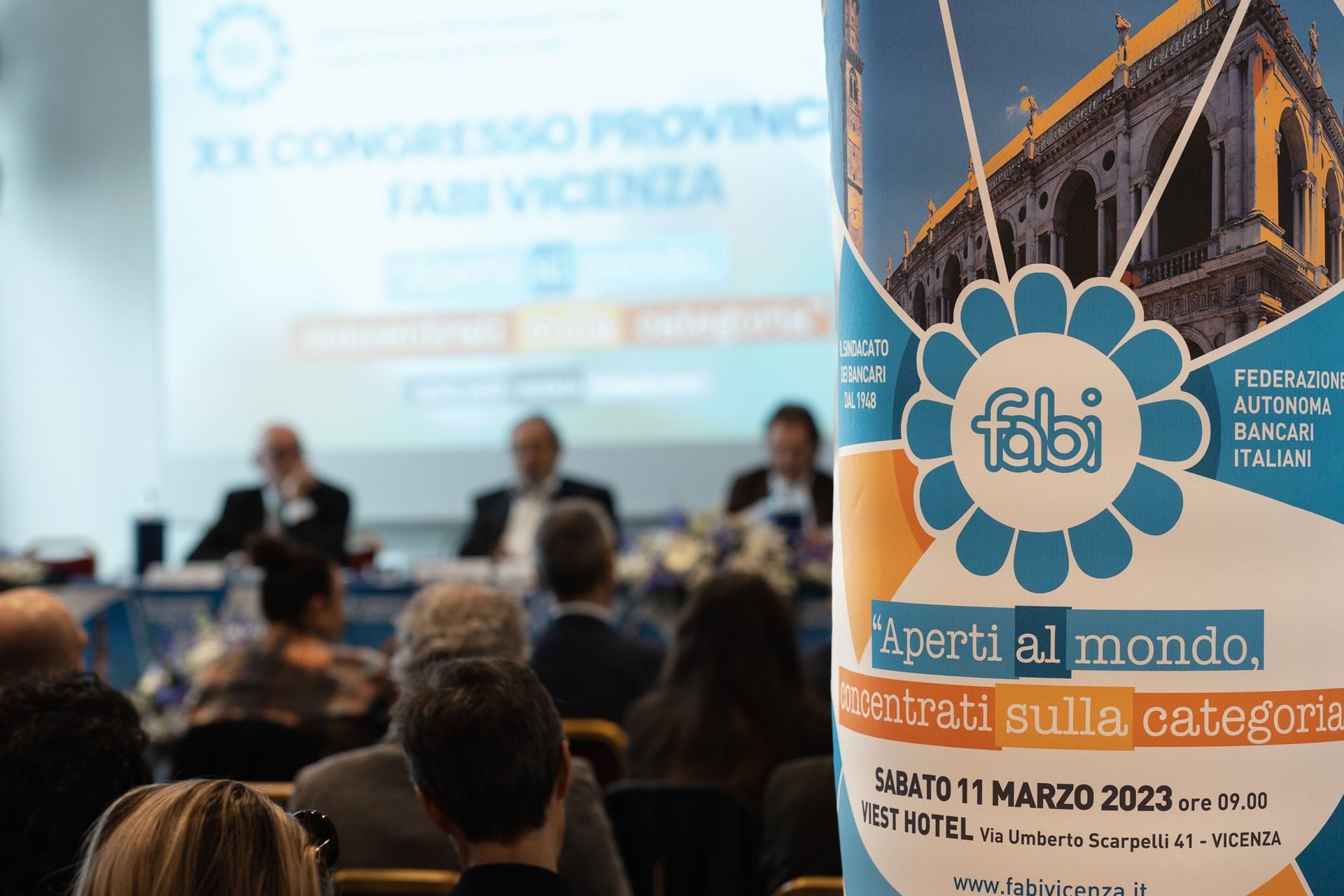 Un gruppo di persone è seduto davanti ad un cartello con la scritta fabi