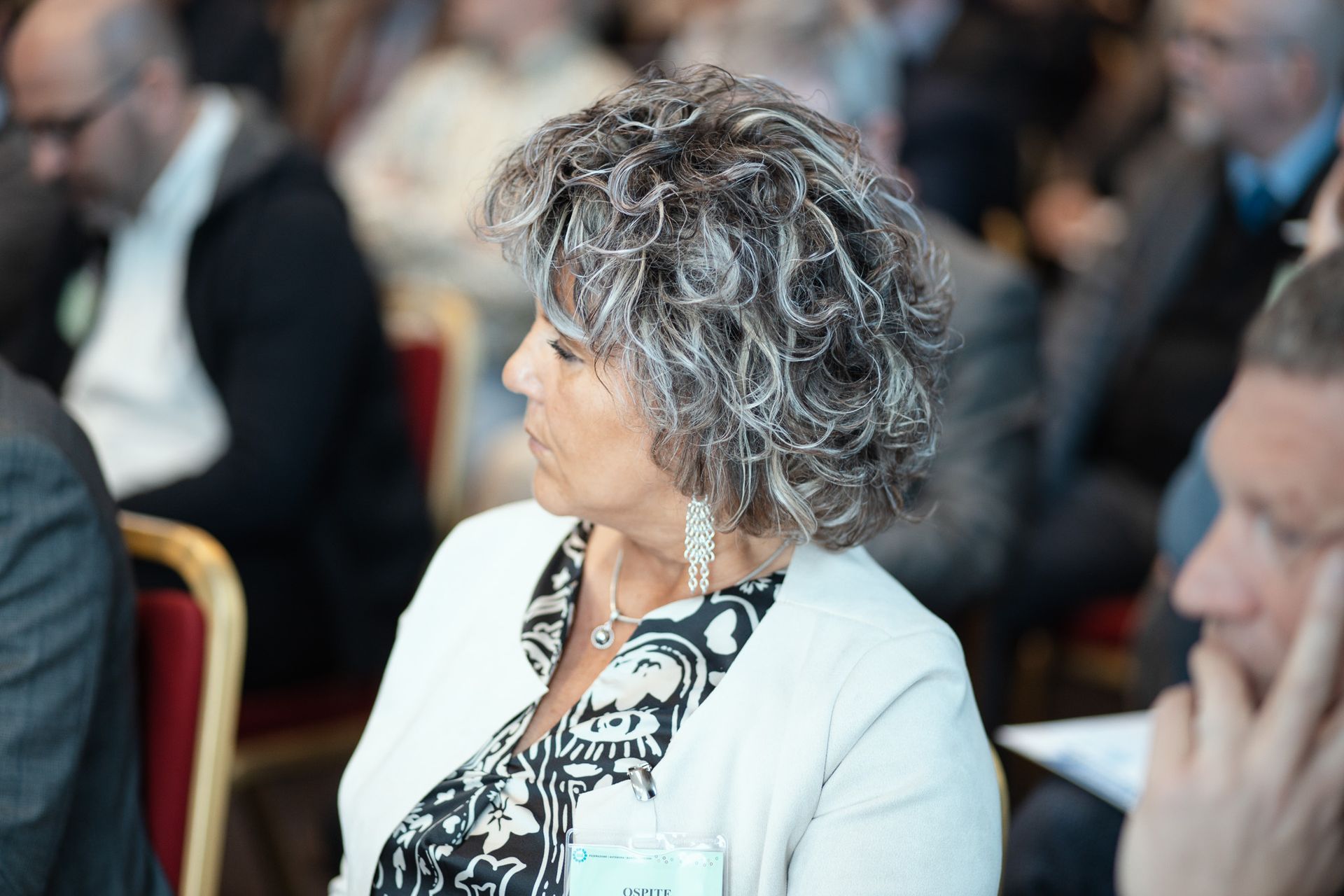 Una donna con i capelli ricci è seduta in mezzo a una folla di persone.