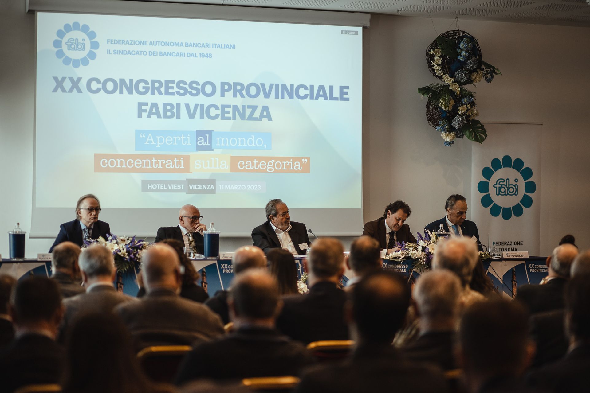 Un gruppo di persone è seduto davanti allo schermo di un proiettore durante una conferenza.