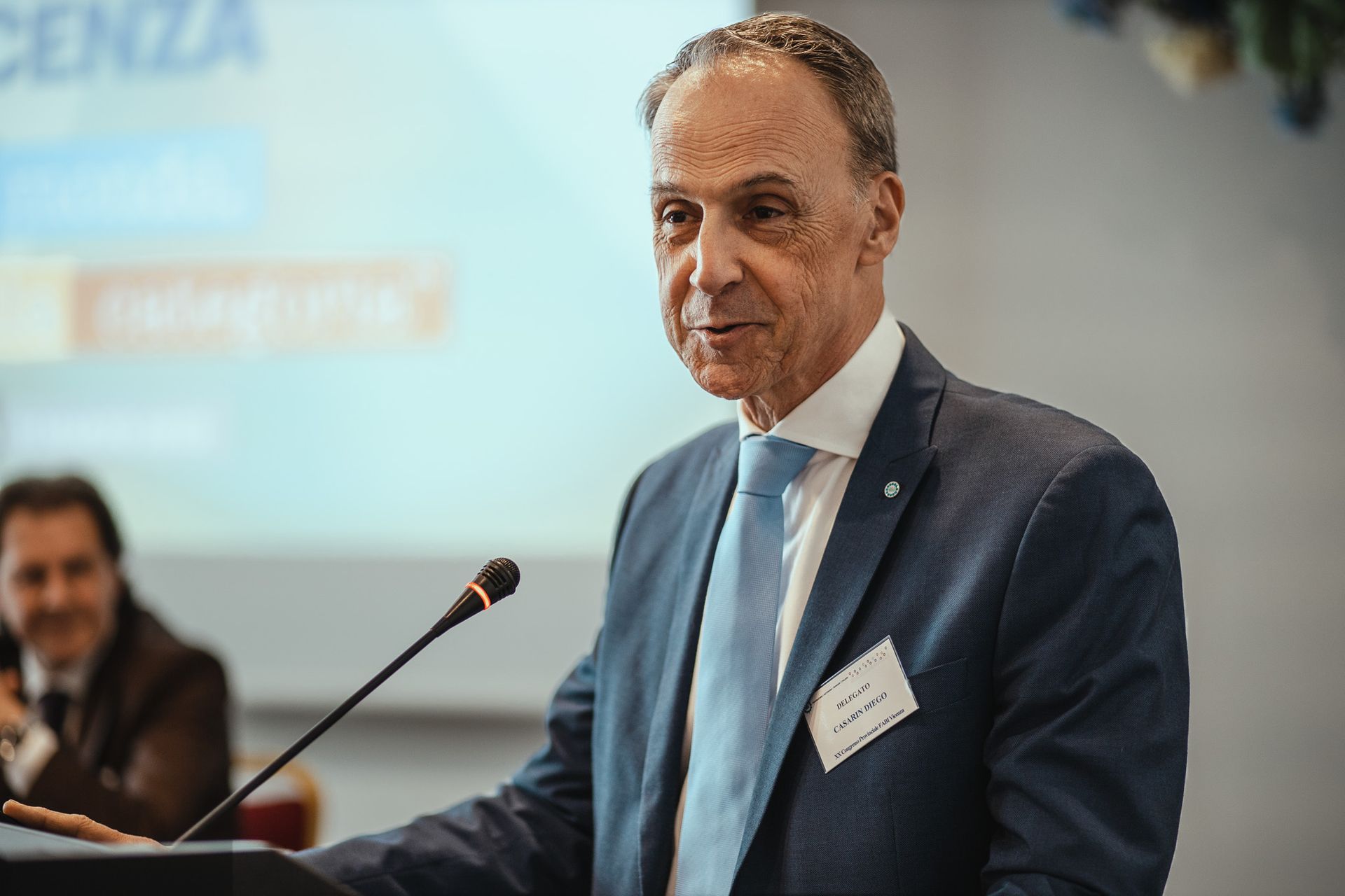 Un uomo in giacca e cravatta parla al microfono.