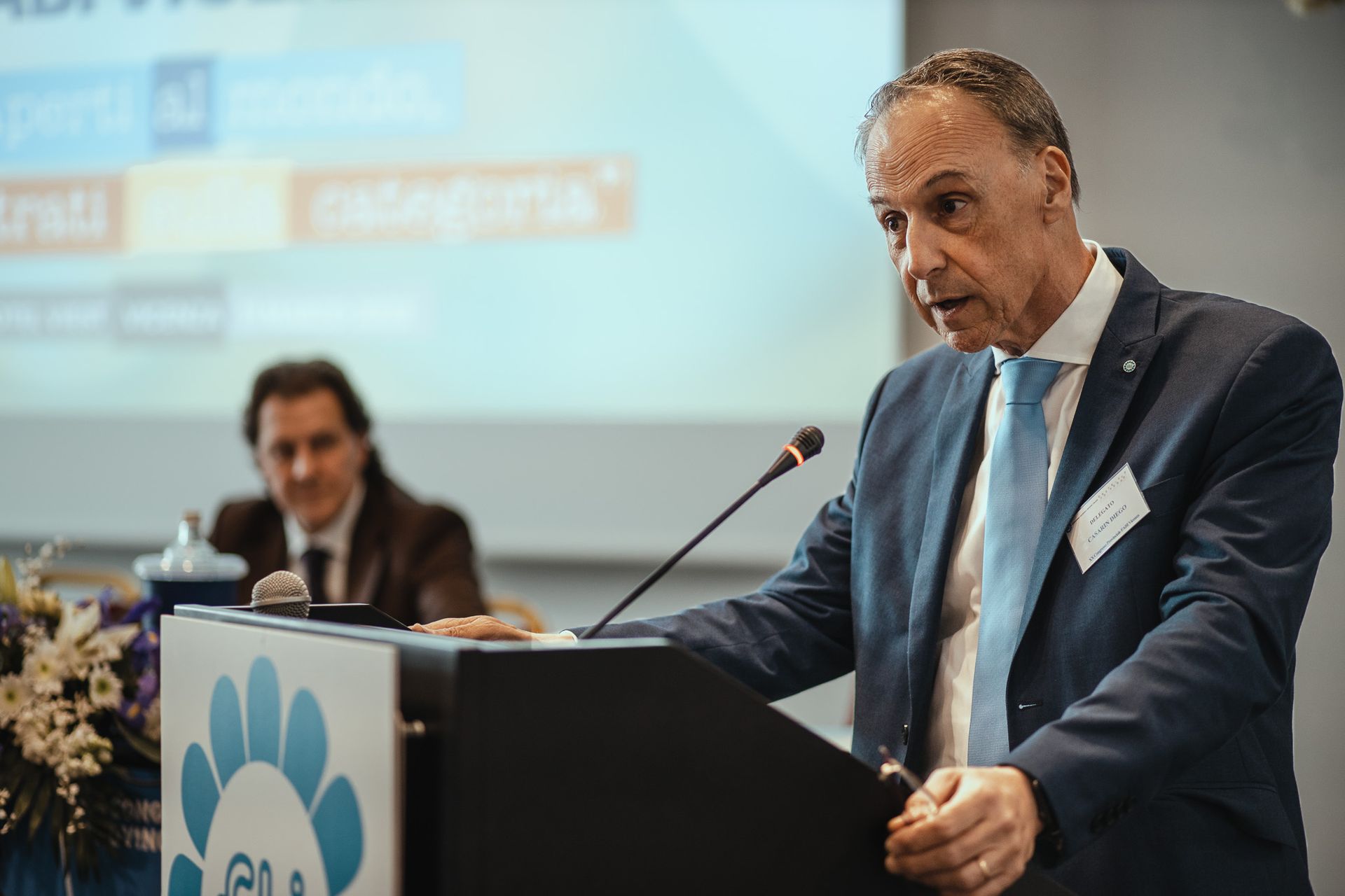 Un uomo in giacca e cravatta è in piedi su un podio e tiene un discorso.