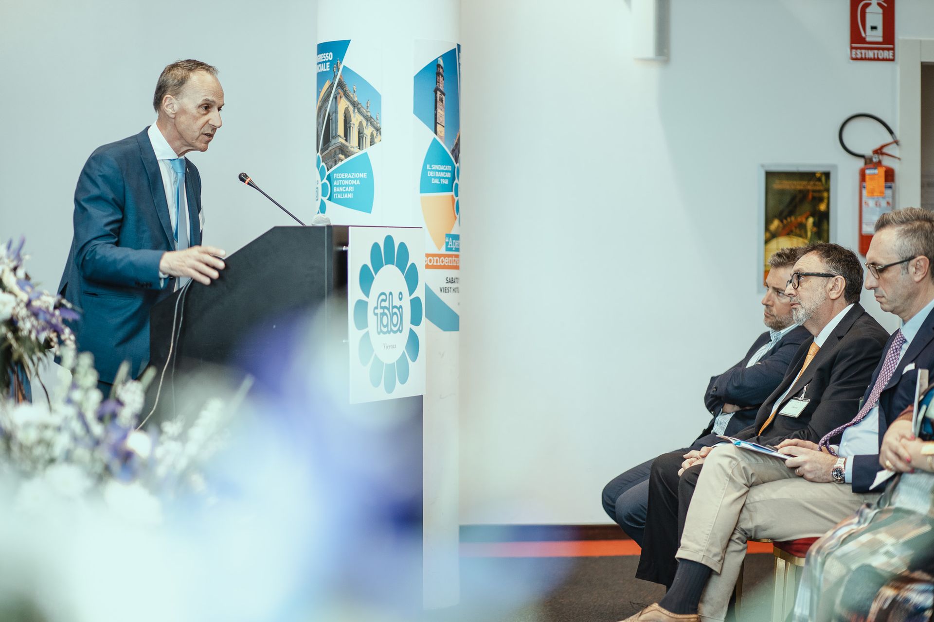 Un uomo è in piedi su un podio e tiene un discorso davanti a un gruppo di persone.