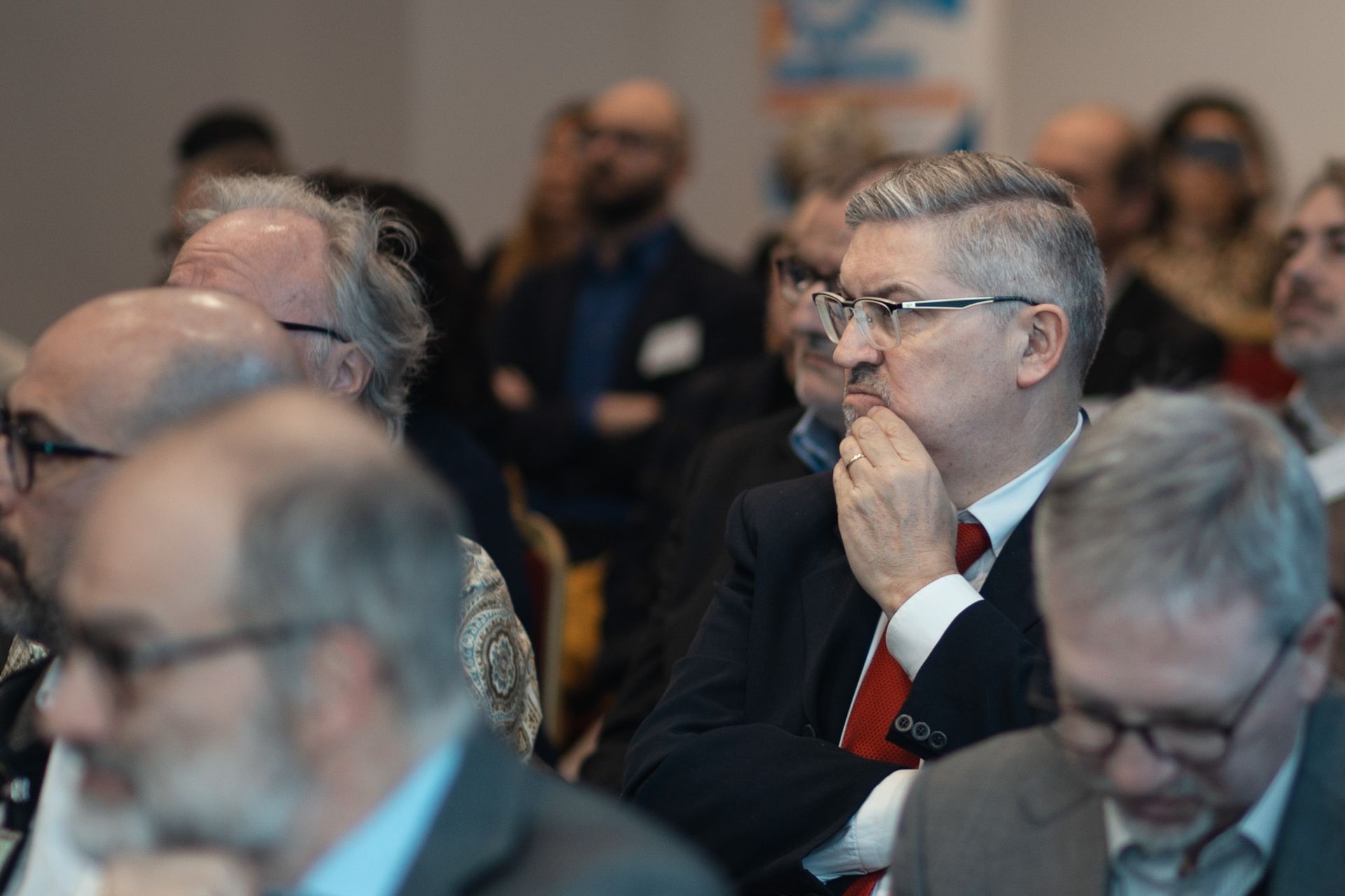 Un uomo in giacca e cravatta è seduto in mezzo a una folla di persone.