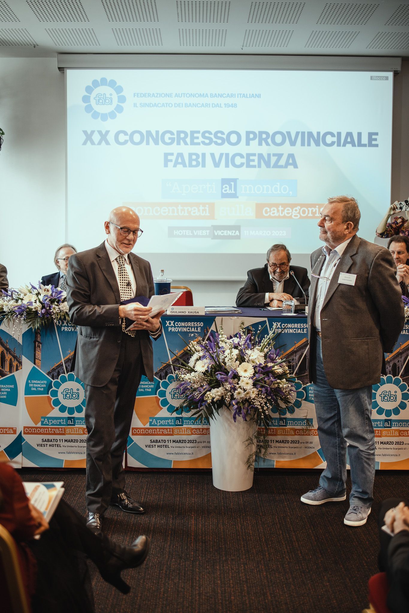 Due uomini sono in piedi davanti allo schermo di un proiettore durante una conferenza.