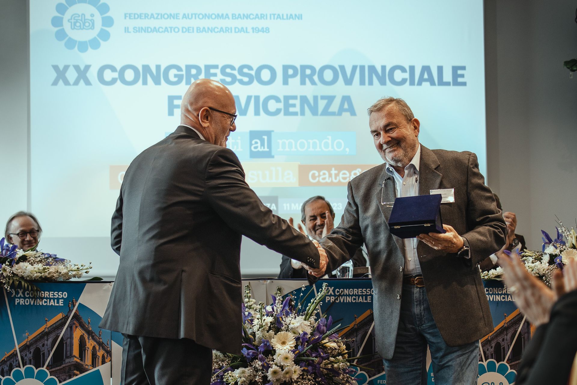 Due uomini si stringono la mano davanti allo schermo di un proiettore.