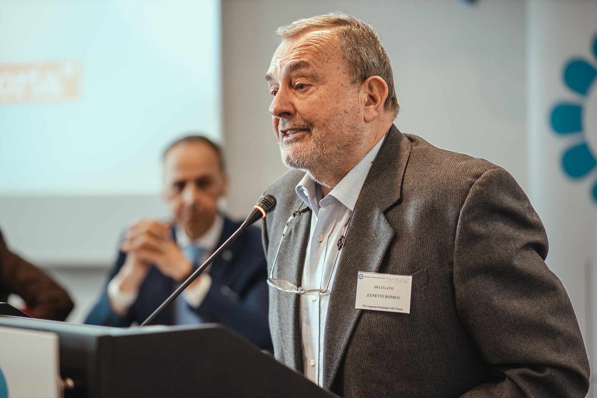 Un uomo in giacca e cravatta è in piedi su un podio e parla al microfono.