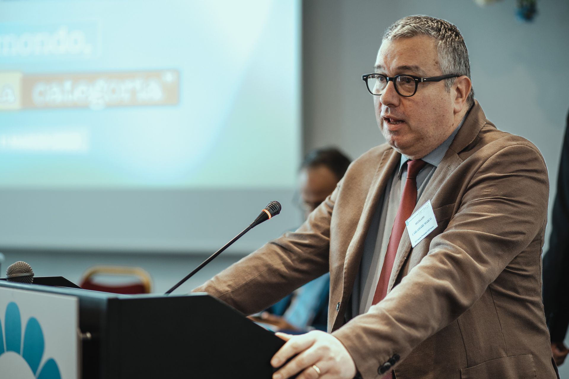 Un uomo in giacca e cravatta tiene un discorso su un podio.