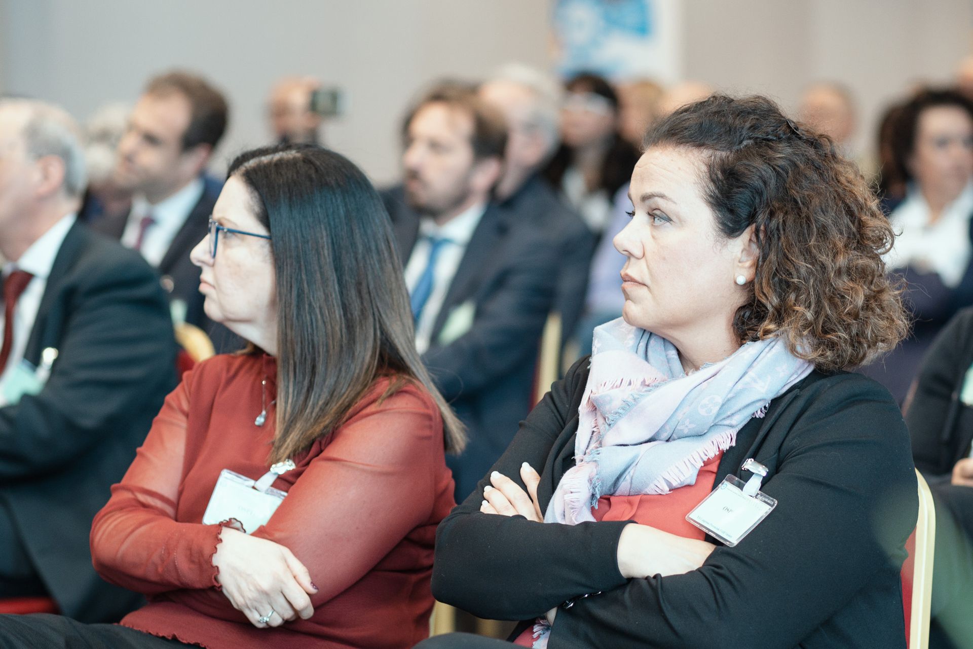 Due donne sono sedute in una stanza con le braccia incrociate.