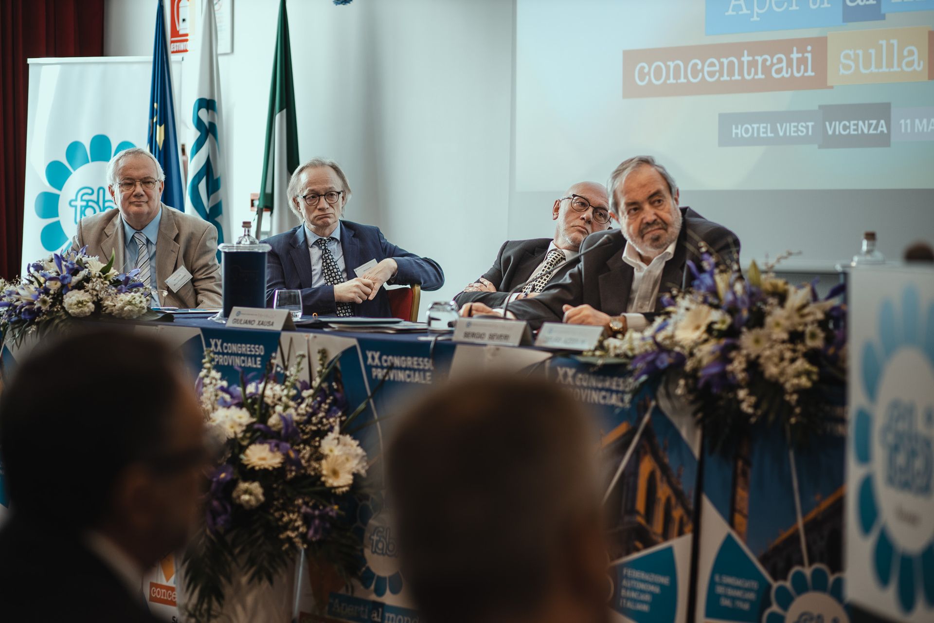 Un gruppo di uomini è seduto a un tavolo davanti a un podio.