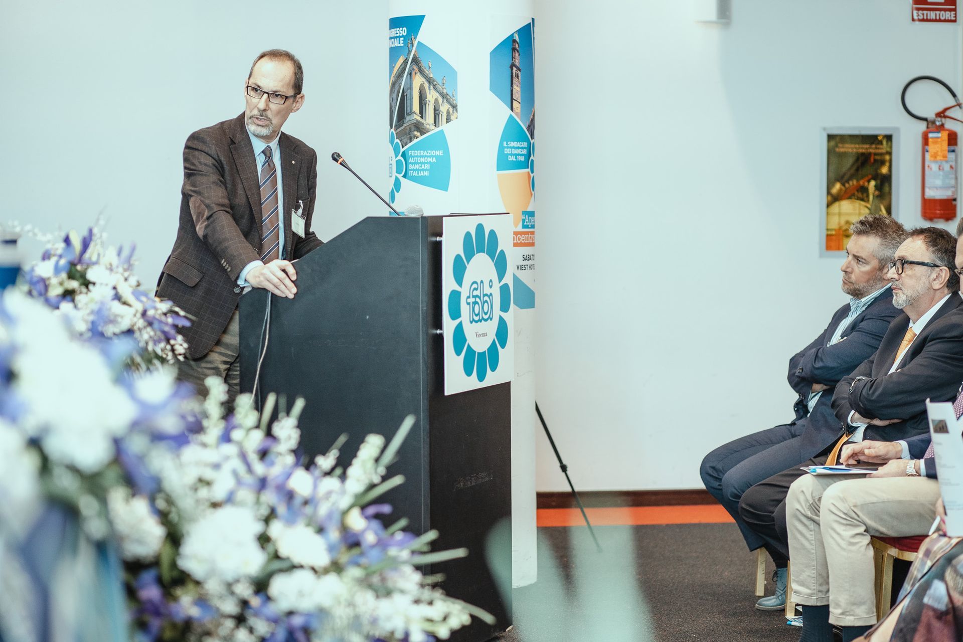 Un uomo è in piedi su un podio e fa una presentazione a un gruppo di persone.