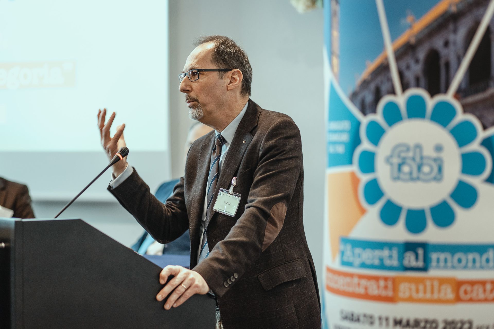 Un uomo in giacca e cravatta tiene un discorso su un podio davanti a un cartello che dice fabi