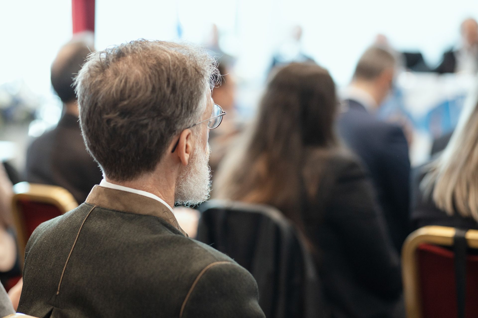 Un uomo con la barba è seduto in una sala conferenze con altre persone.