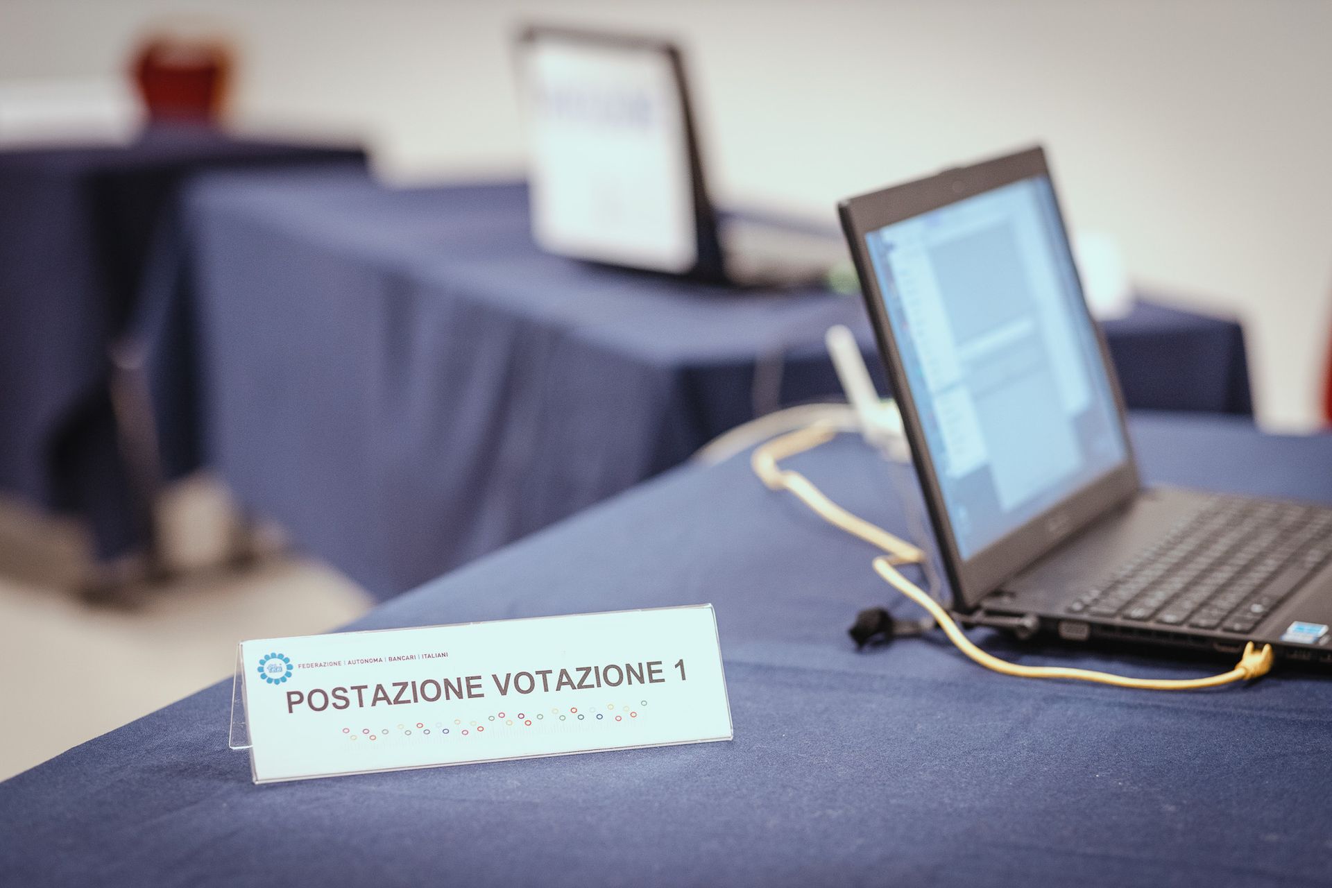Un laptop è appoggiato su un tavolo accanto a un cartello che dice postazione votazione 1