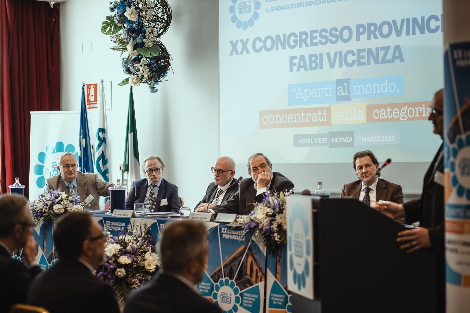 Un gruppo di uomini è seduto a un tavolo davanti allo schermo di un proiettore.